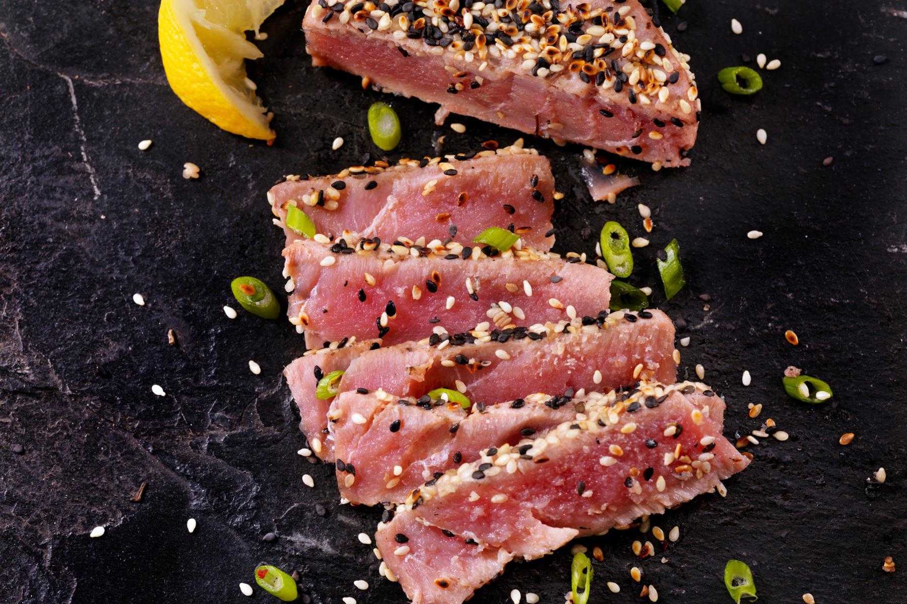 Slices of sesame crusted tuna on black plate.