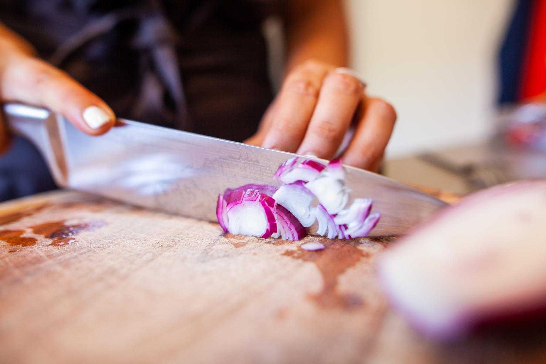 Close-up of hand with knife chopping onions.