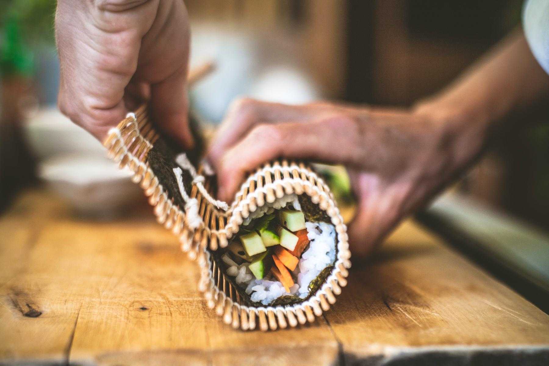 Side view of man rolling sushi roll.