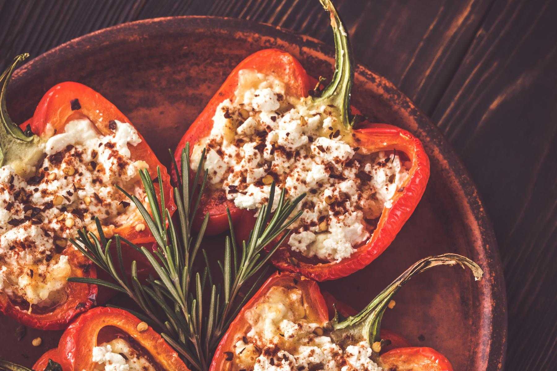 Roasted and stuffed red peppers on wooden tray.