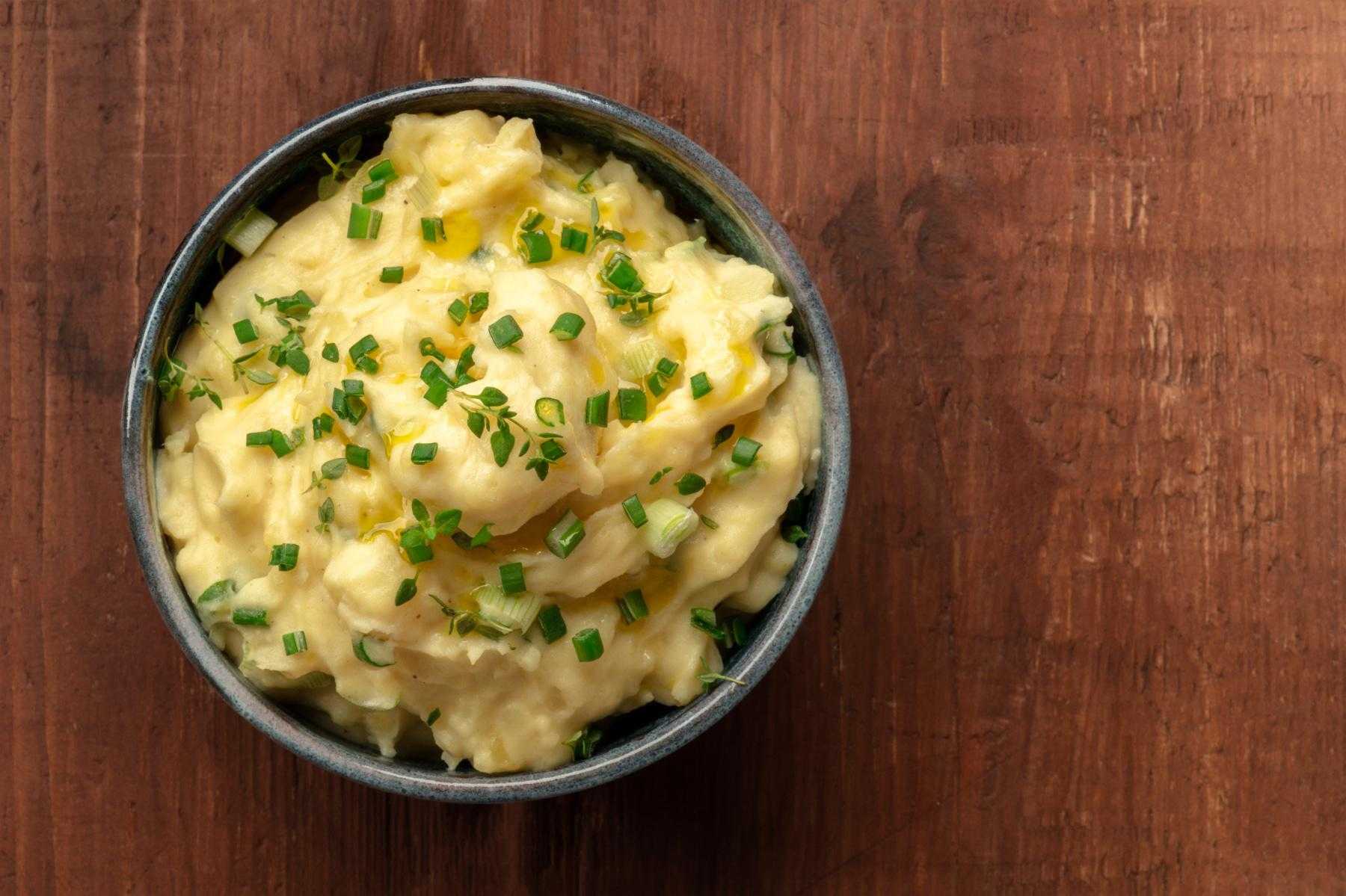 Overhead view of a bowl of scallion mashed potatoes on wooden background.