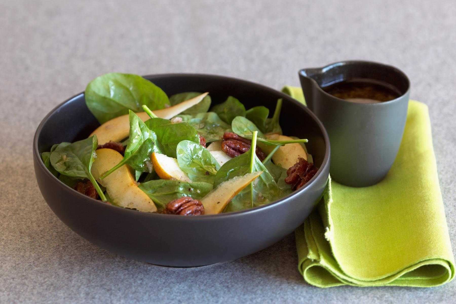 A black bowl filled with a spinach candied pecan salad and a cup of tea.