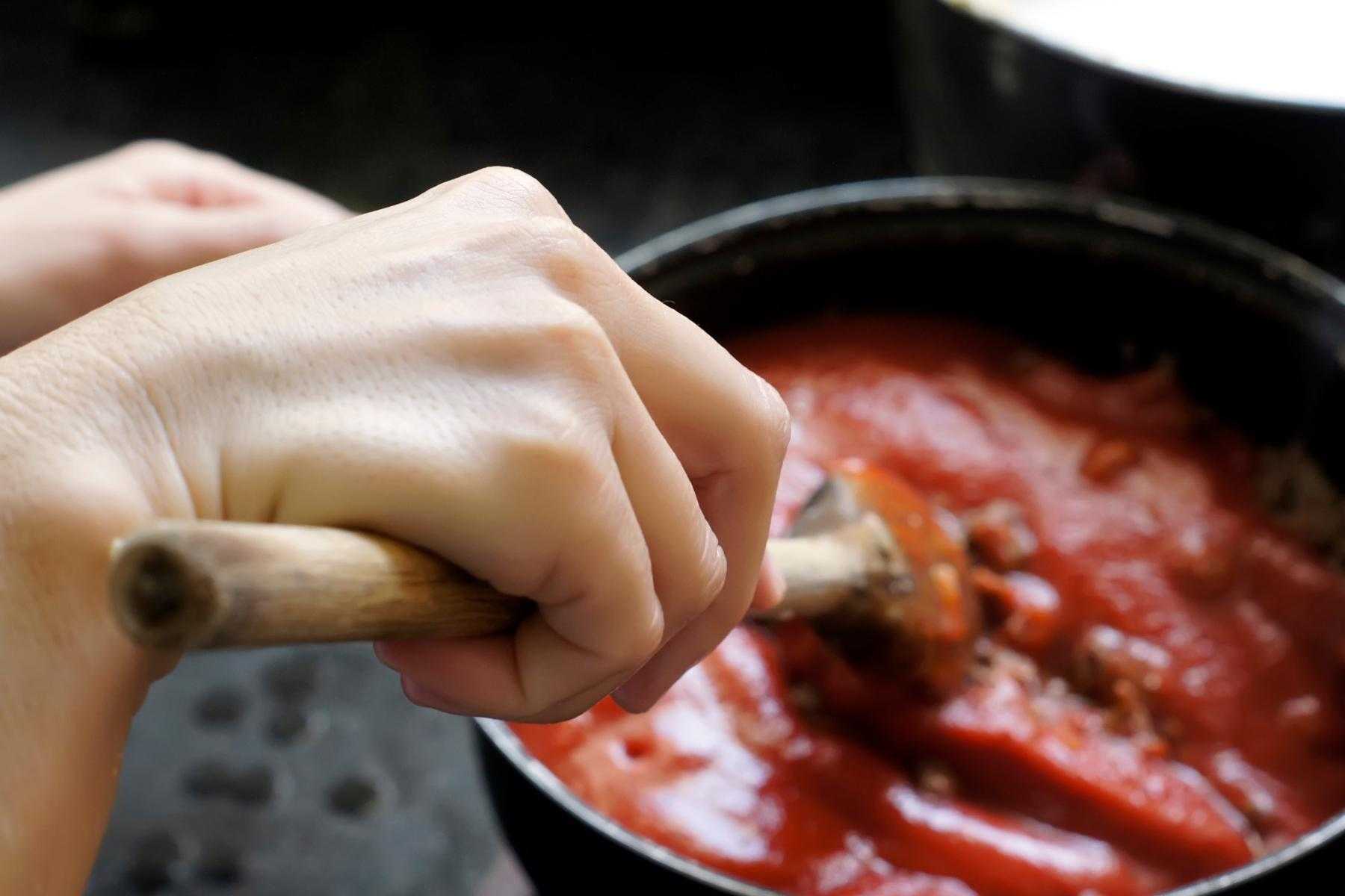 A woman stirring a plum tomato sauce on the stove.