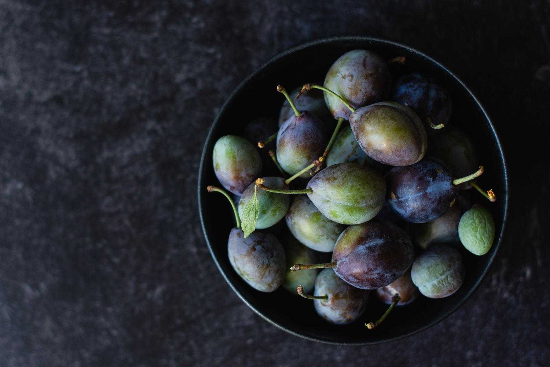 Bowl of fresh plums against dark background.