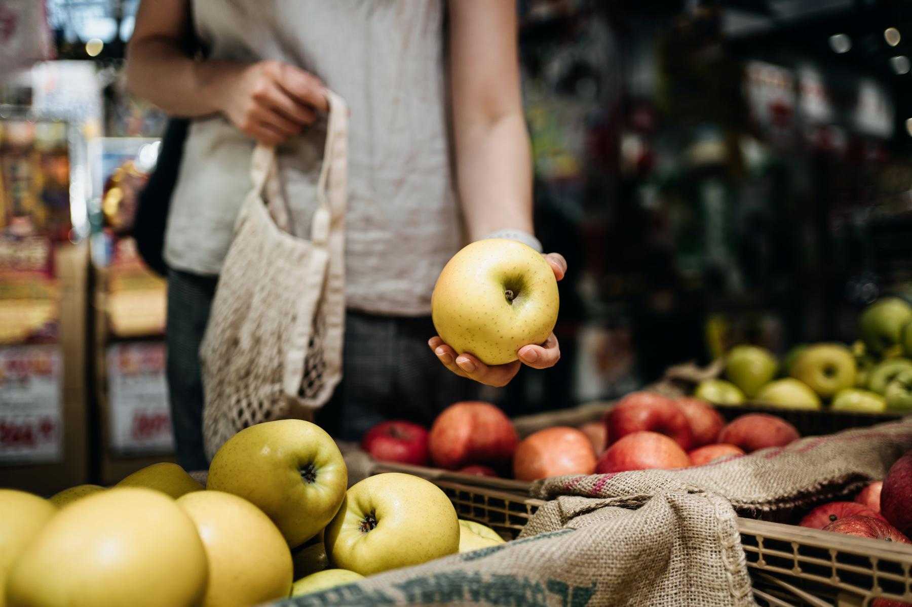 Close-up of woman's hand picking up apple in grocery store.