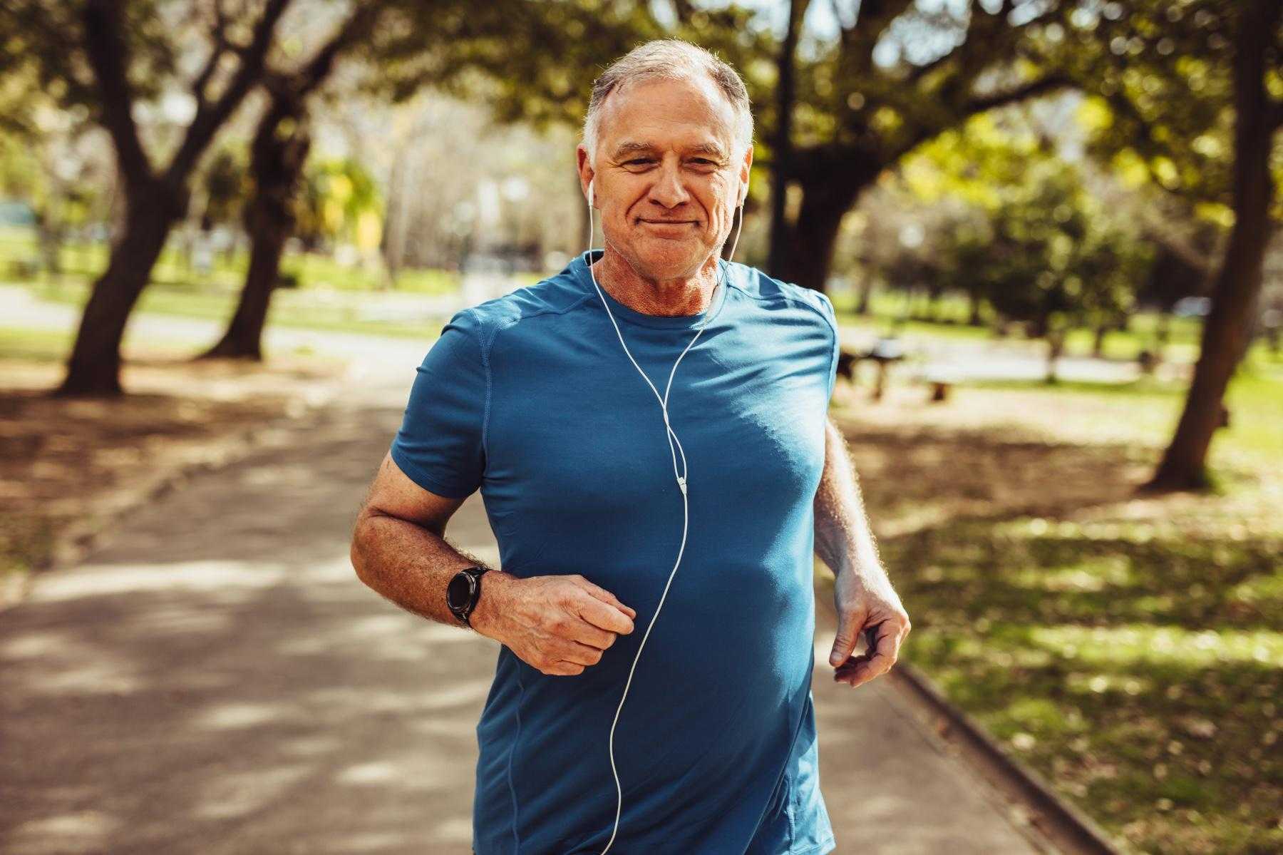 Older man running through park with headphones in.