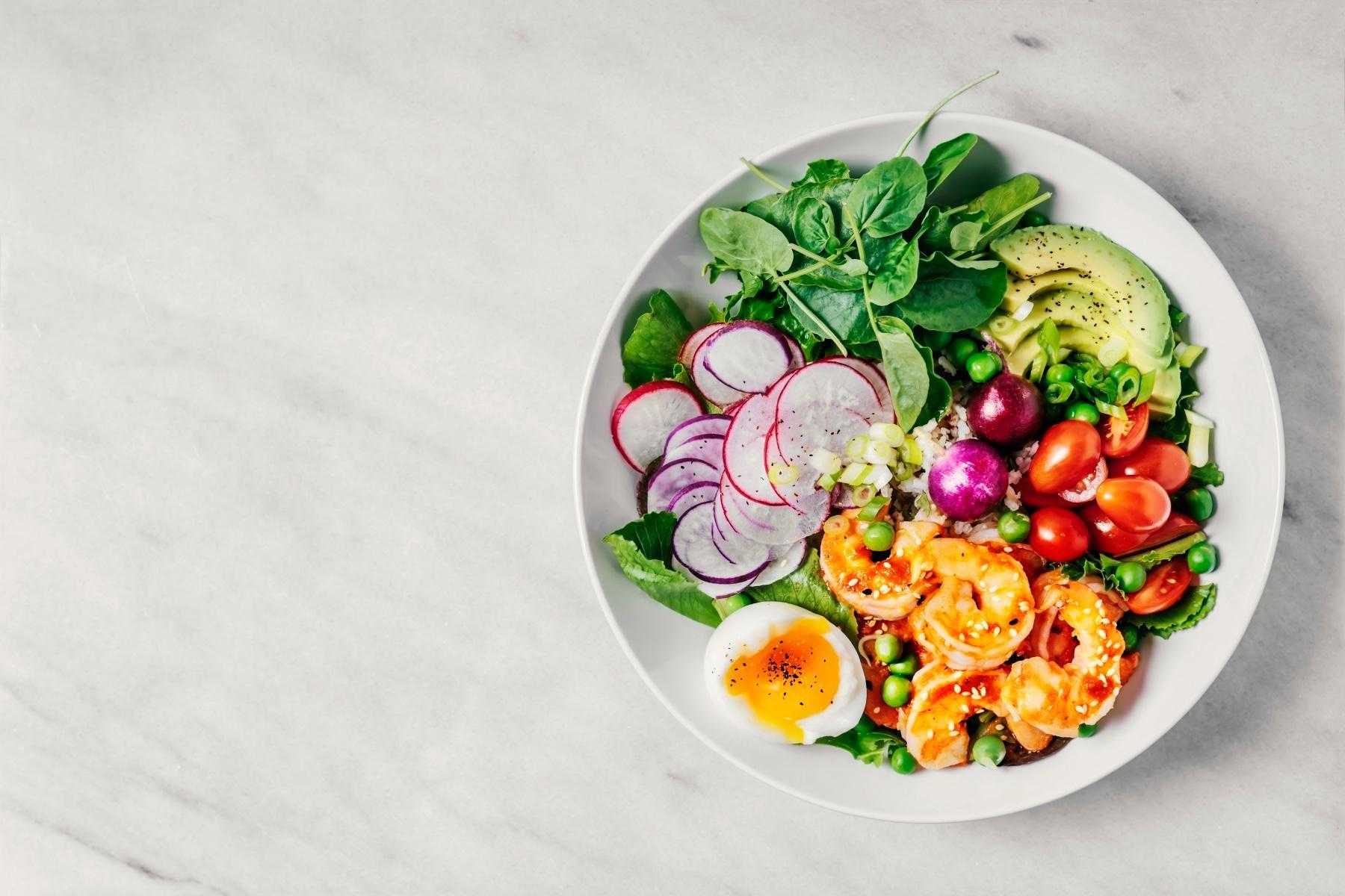 A bowl of salad with avocado, shrimp, radishes, and tomatoes.