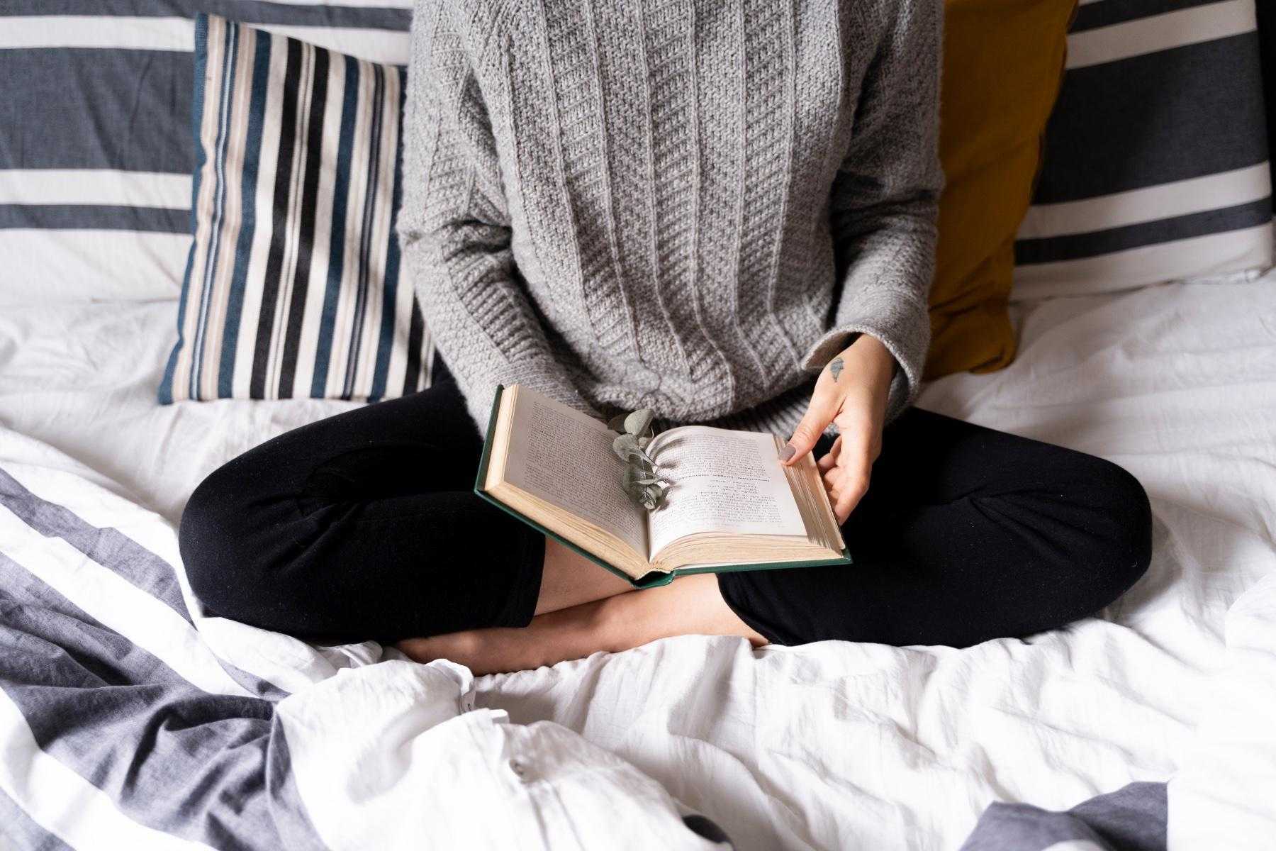 Overhead shot of woman reading book while sitting in bed.