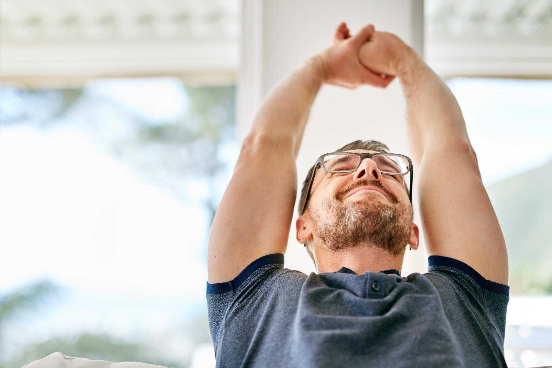 close-up of man from the chest up with arms over head stretching as he leans back