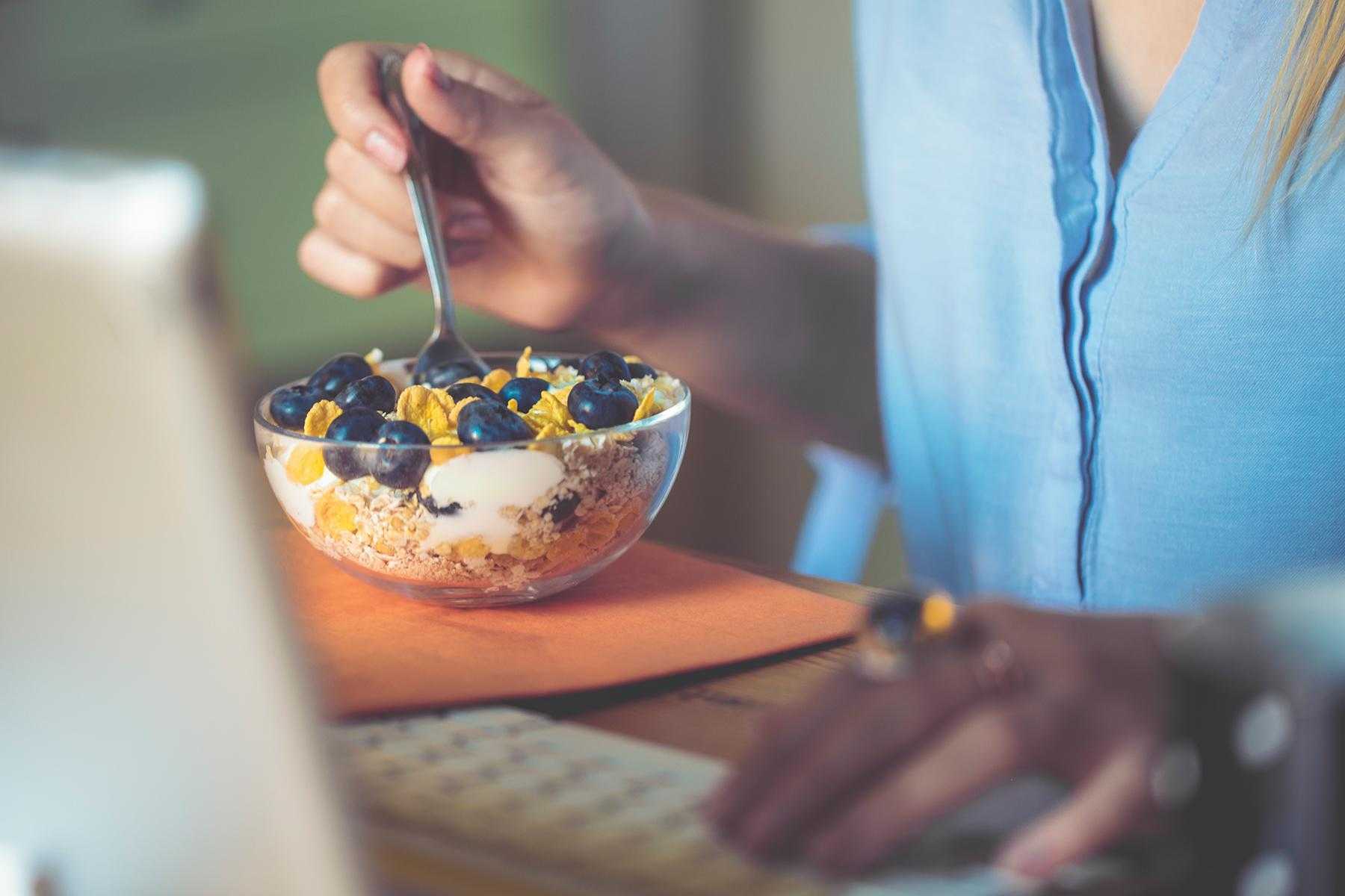 close-up of woman eating bowl of cereal while working on laptop