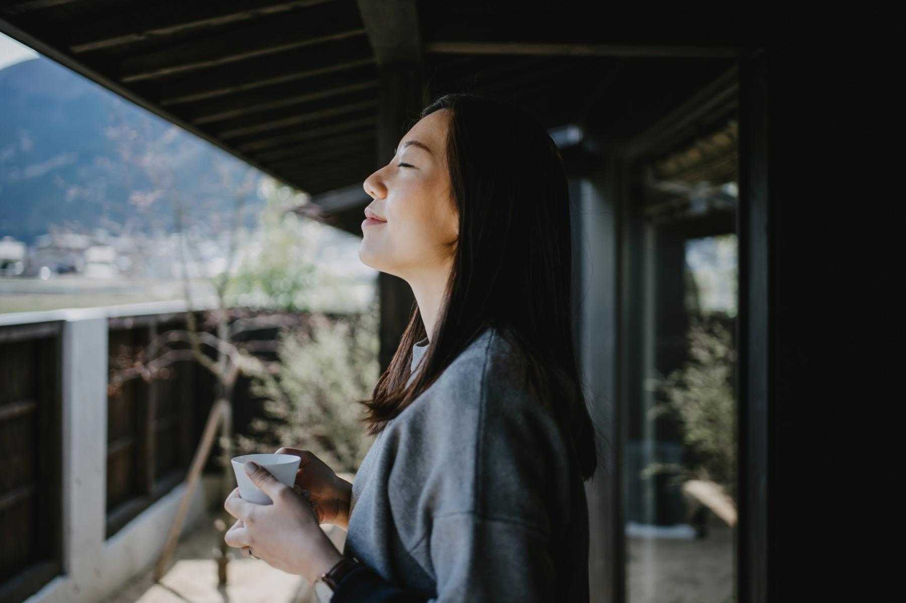 Woman holding a coffee cup on her balcony as she is breathing in the fresh air.
