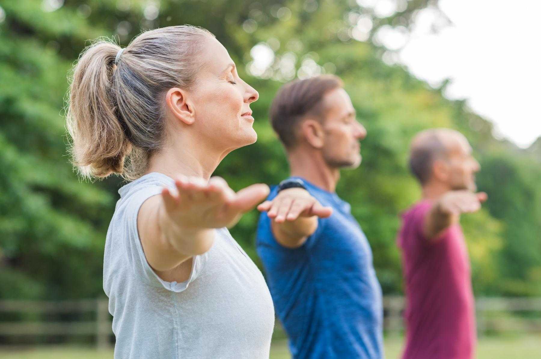 one woman in focus and two men staggered behind her out of focus all with arms out meditating