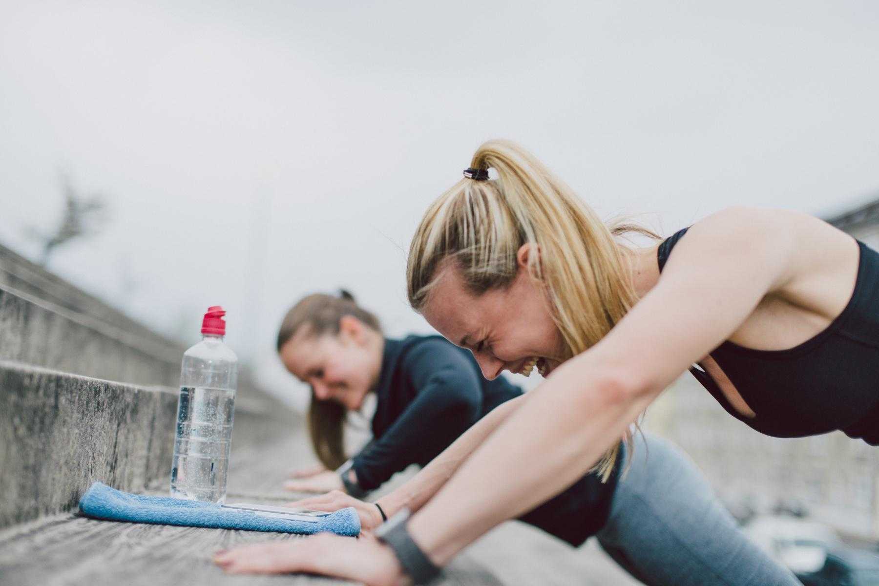 two women laughing while doing push-ups on cement steps outside