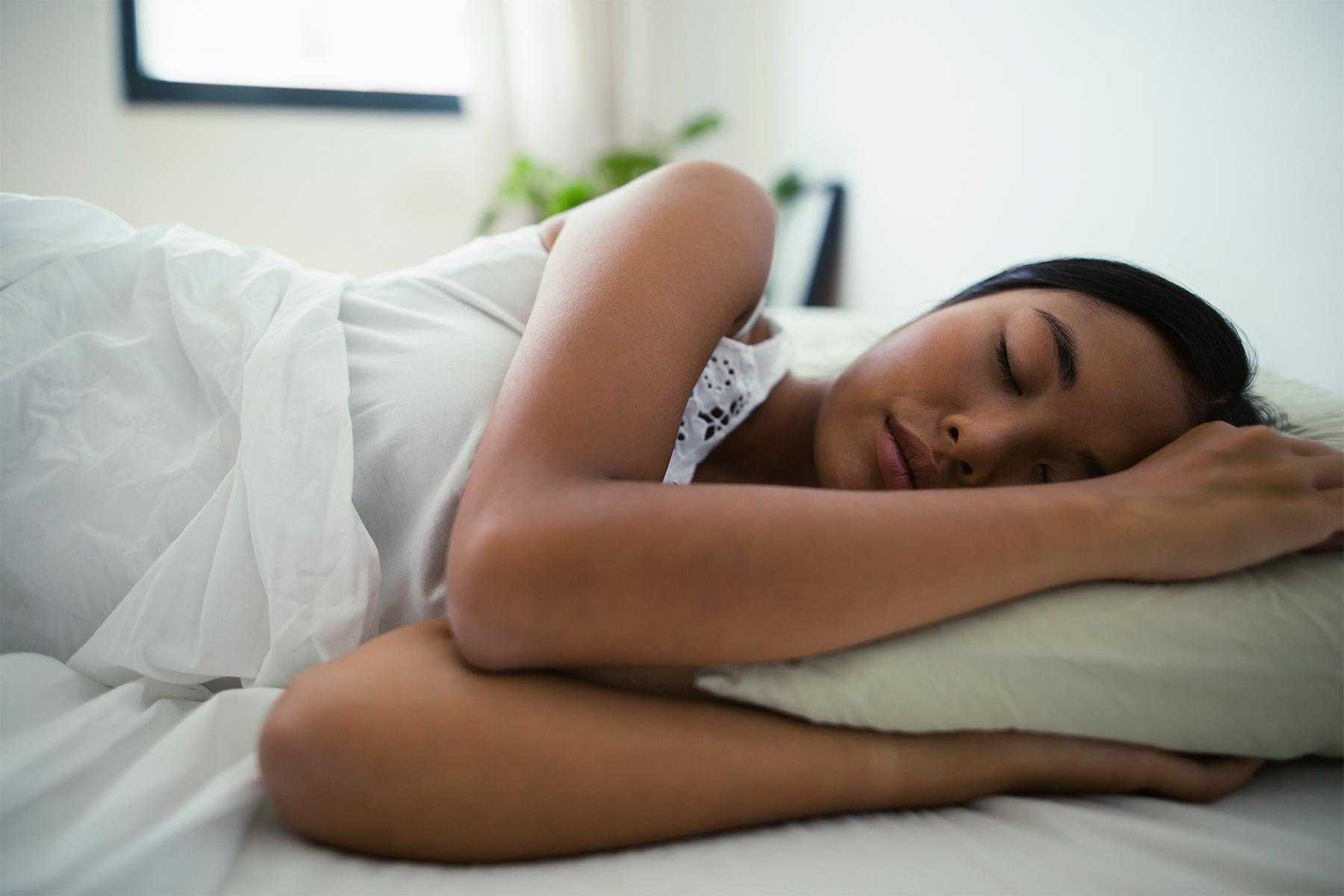 Close-up of woman sleeping in bed with white sheets.