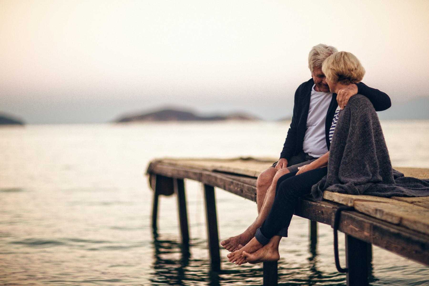 A mature couple sitting on a dock together.