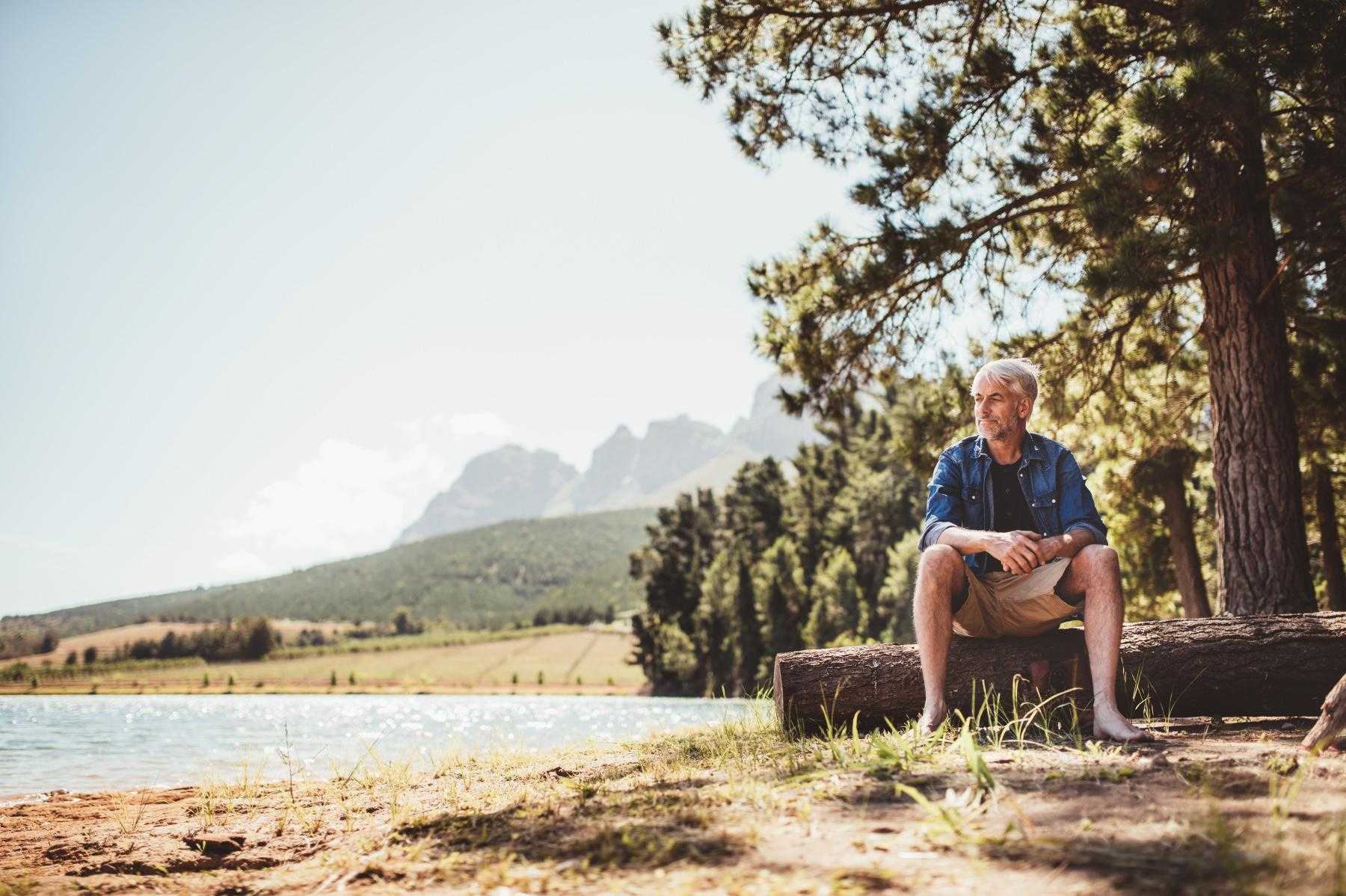 Mature man sitting near a lake looking out into the distance.