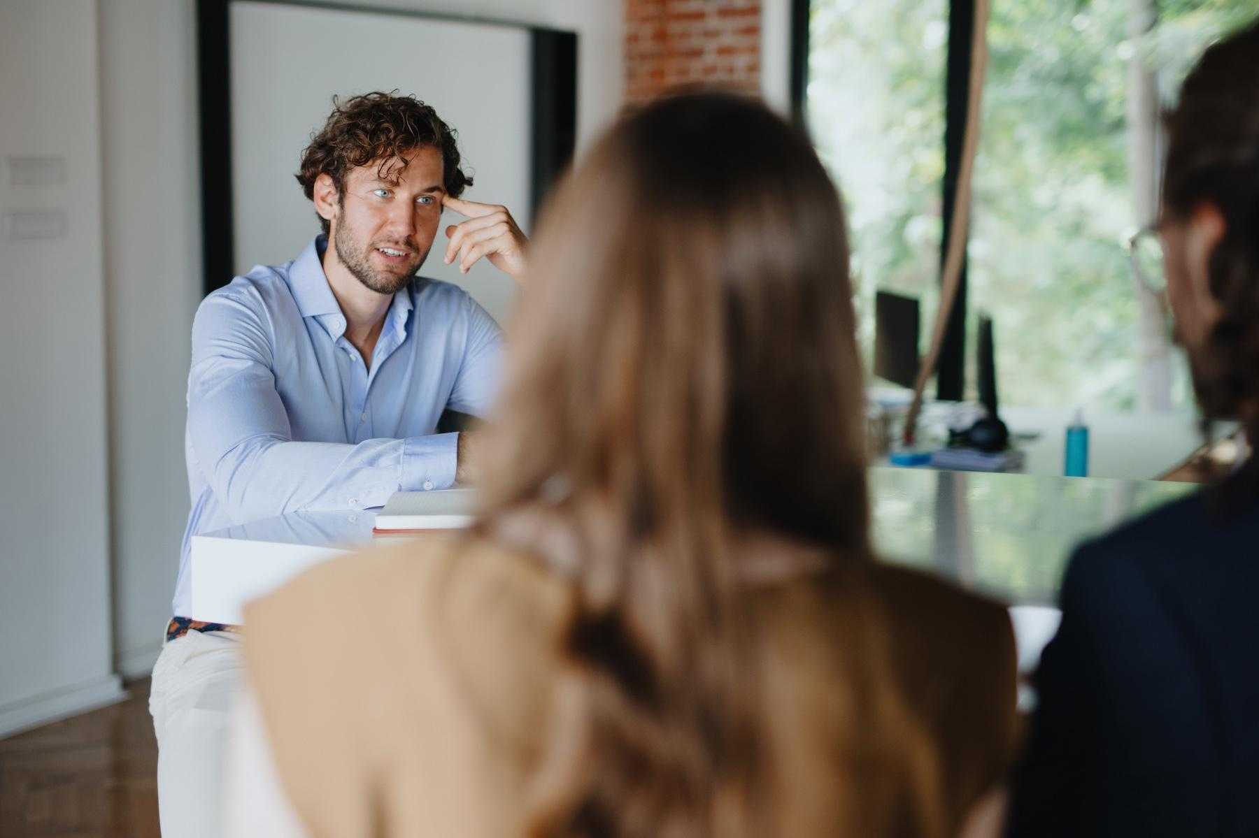 A young man speaking with two female coworkers.