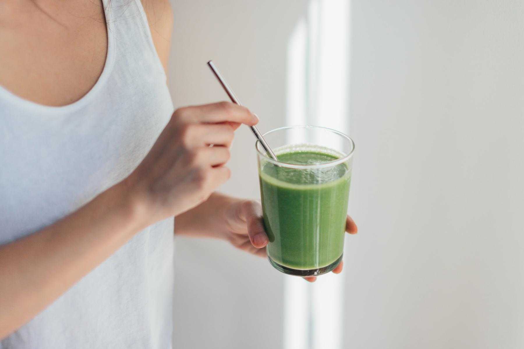 Woman drinking green smoothie in glass with metal straw.