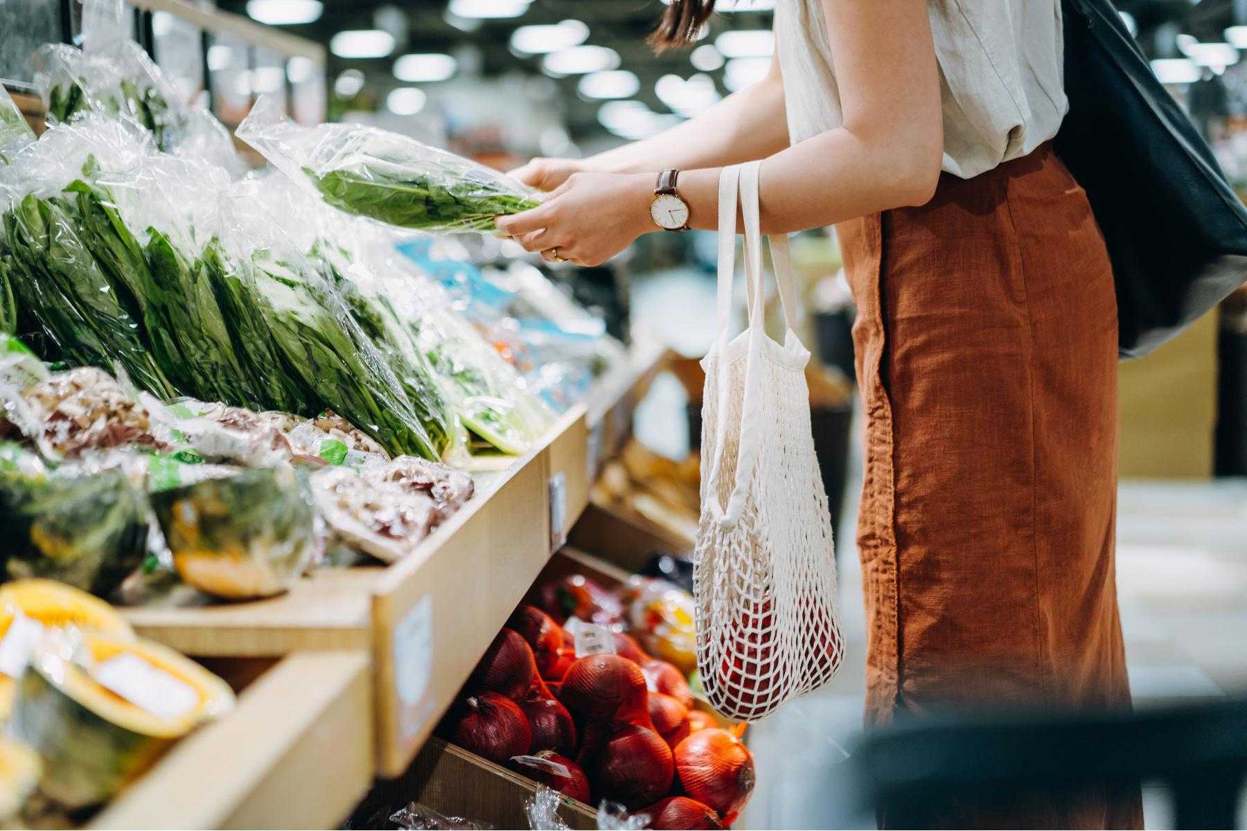 sideview of woman from neck down shopping in the produce section of a grocery store