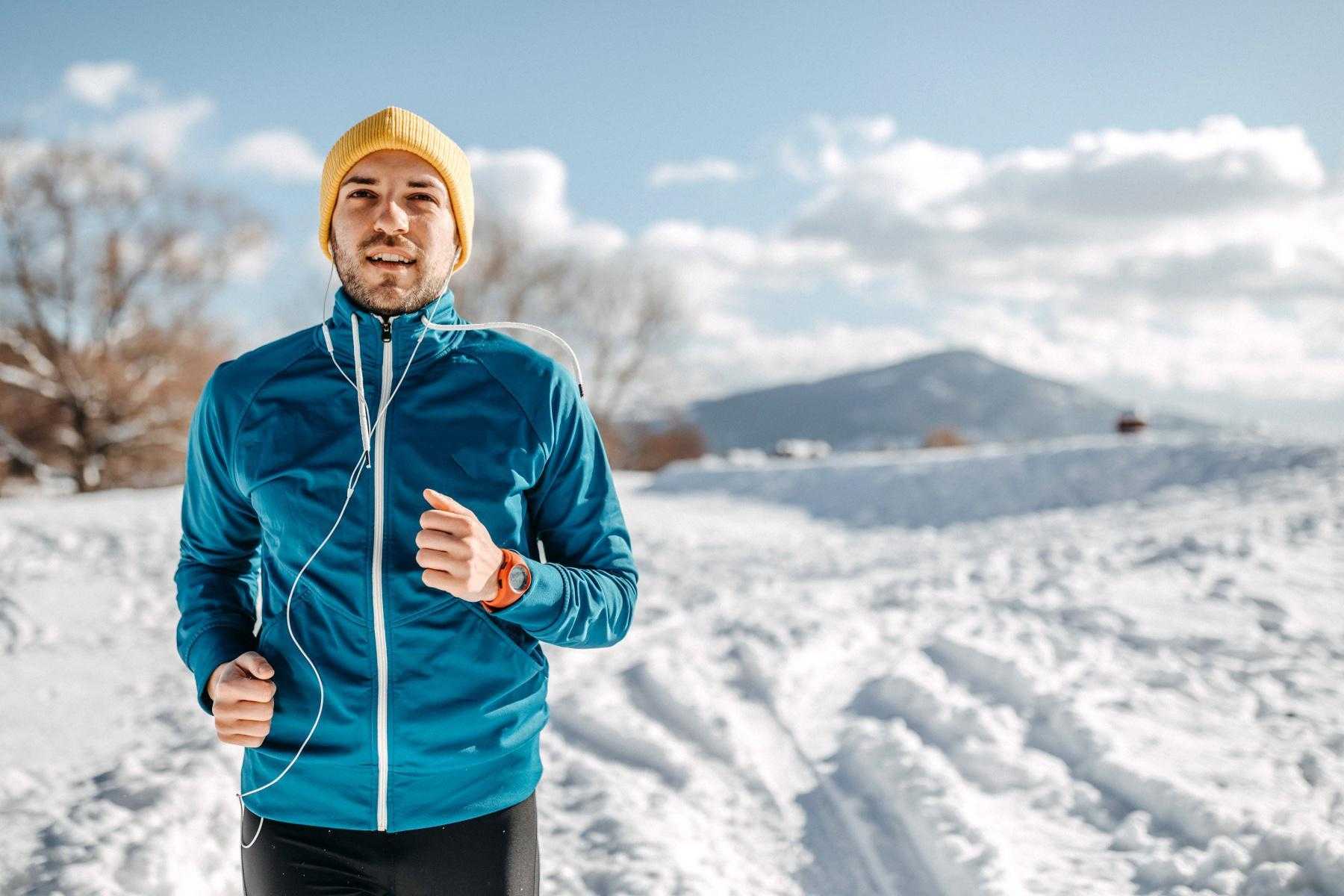 man in blue coat and yellow hat running in snow with headphones on