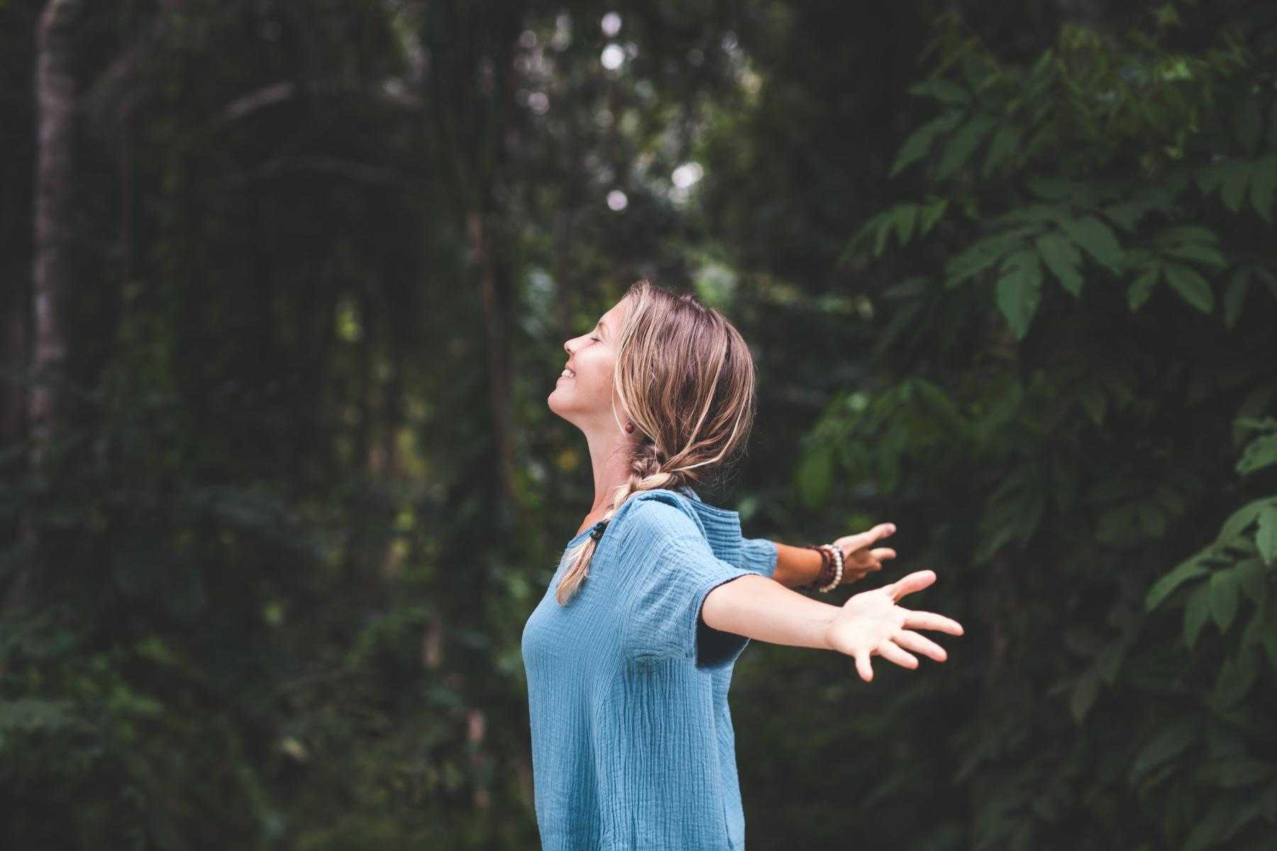 Woman standing in the forest and looking up at the sky.