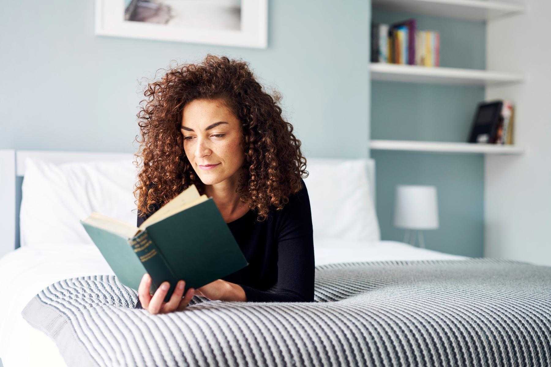 Woman laying on her bed reading a book.