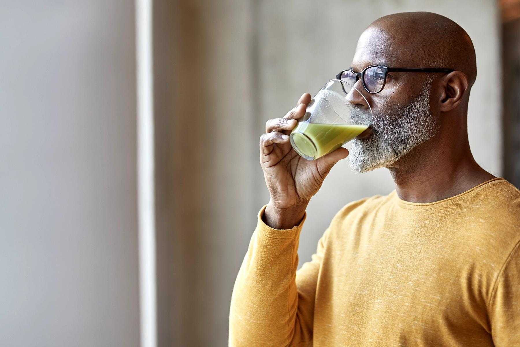 Man drinking green smoothie while looking out window.