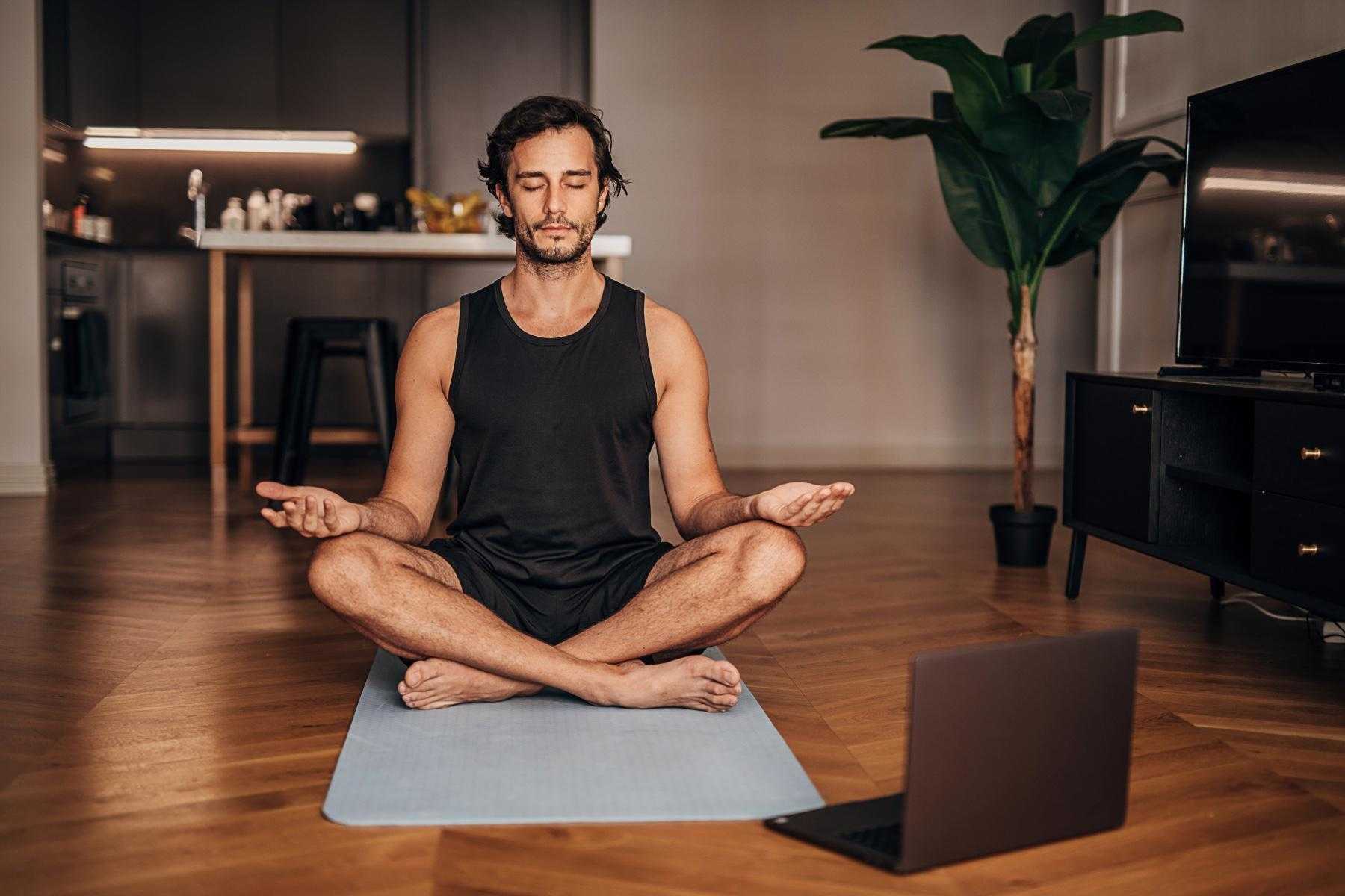 man mediating on yoga mat with computer in front of him