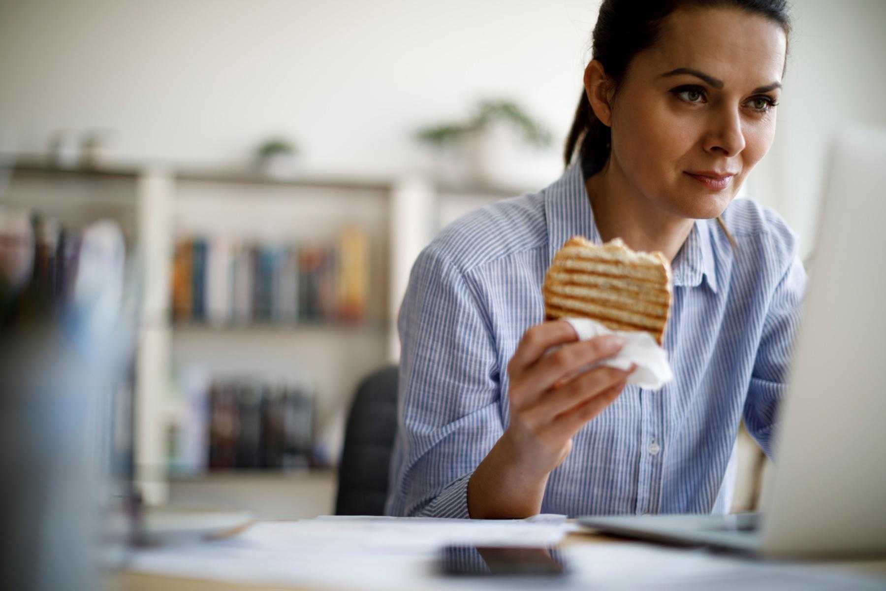 woman eating sandwich while working on laptop