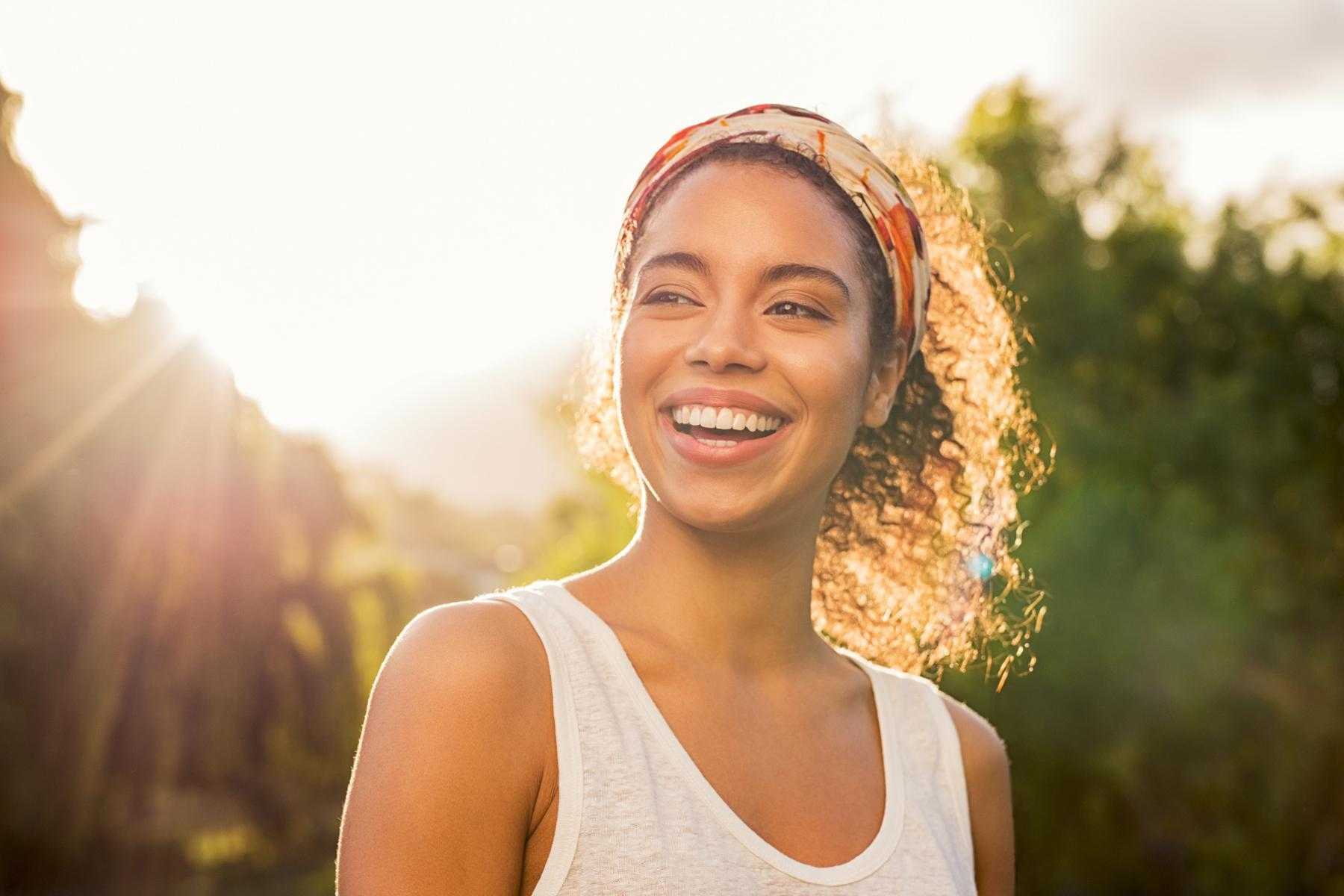 A young woman smiling with the sun behind her.