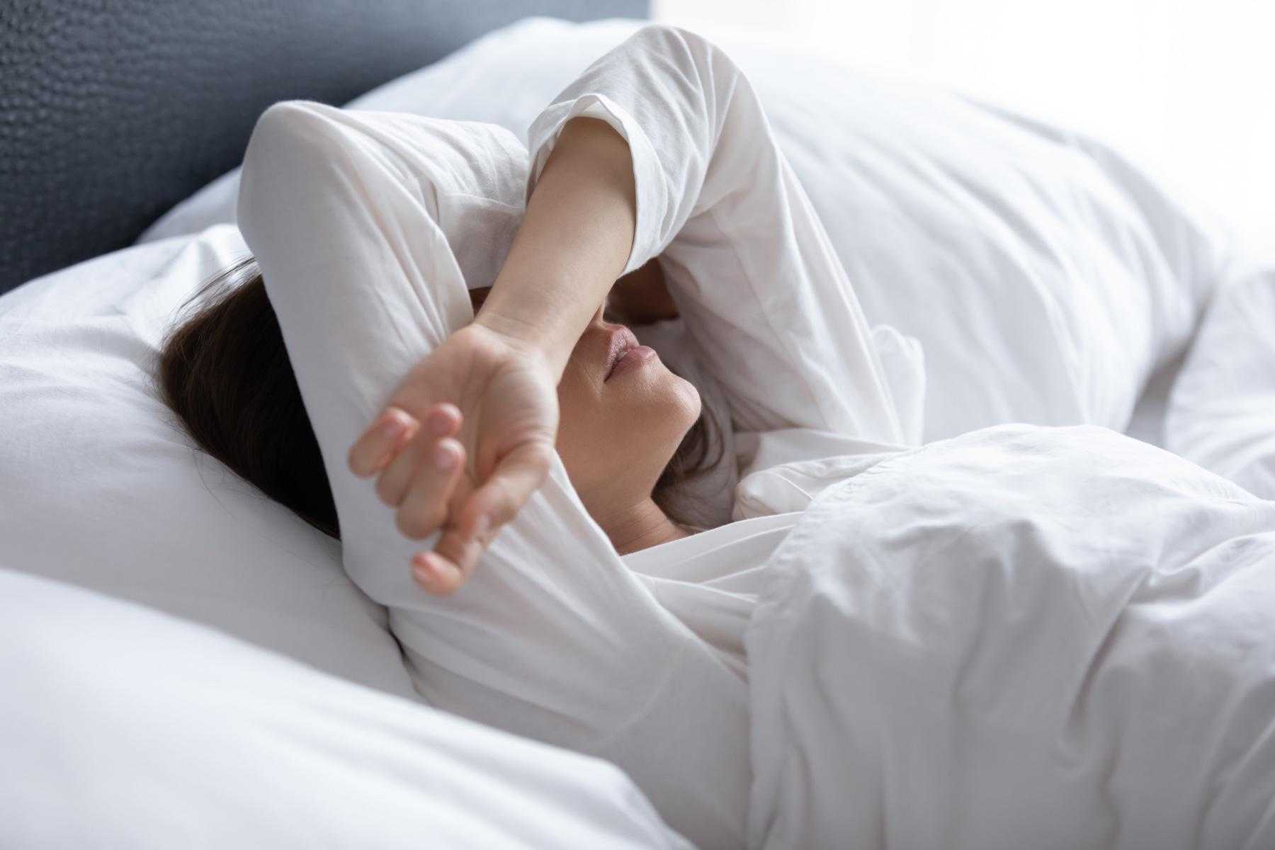 Woman laying in bed with arms over eyes.
