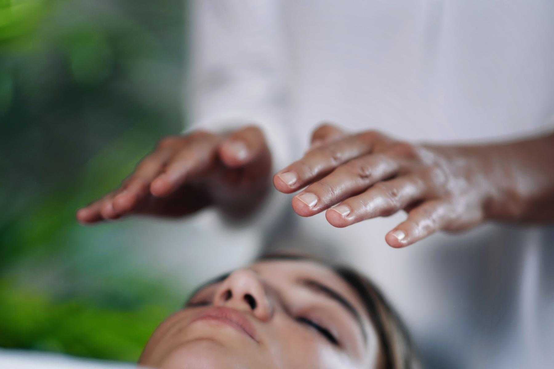 close-up of hands hovering above woman's face during a healing energy treatment