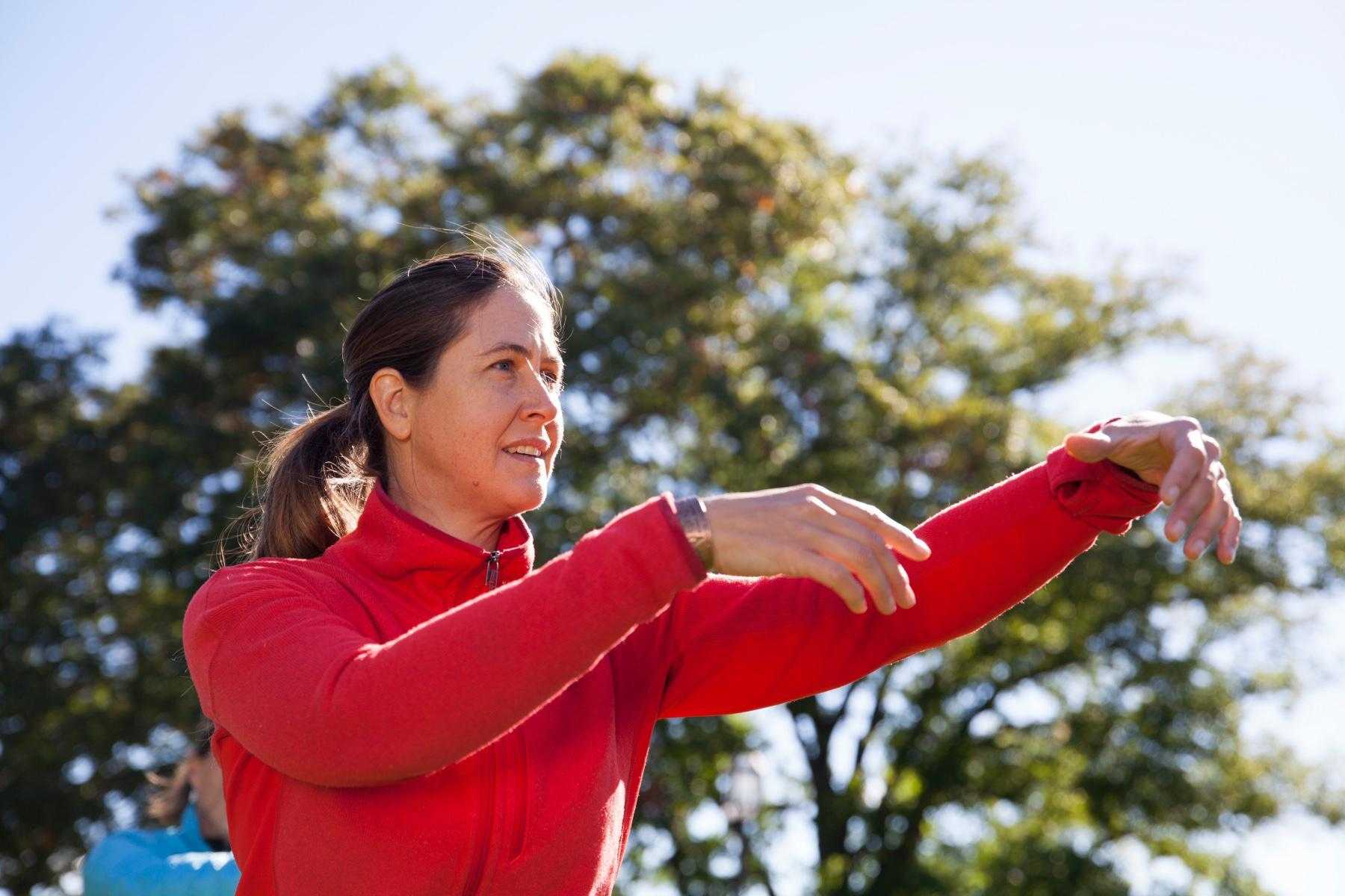 woman from waist up wearing a red a jacket with arms up doing qi gong