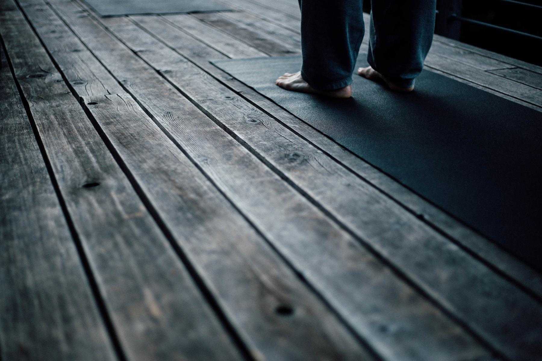 close-up of feet standing on yoga mat on wooden deck