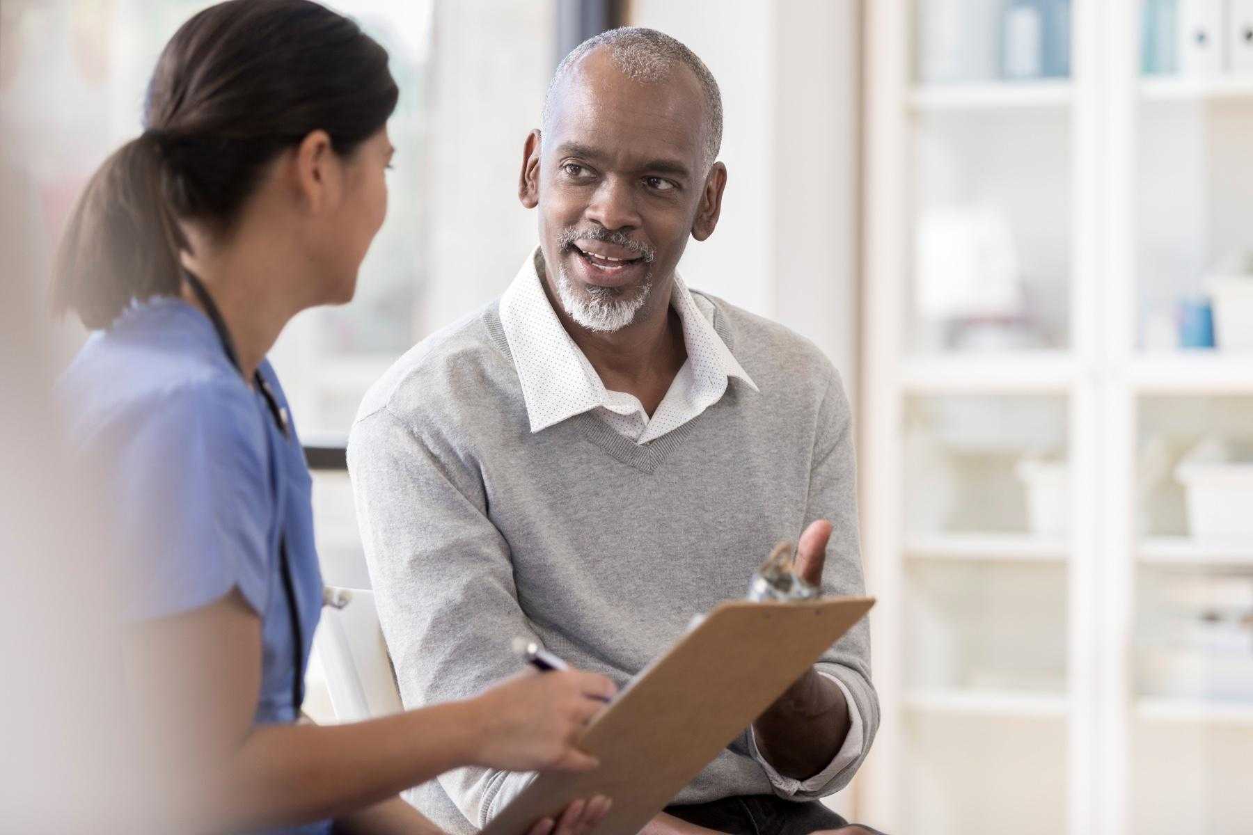 Older man having a conversation with a doctor about results on clipboard in front of them.