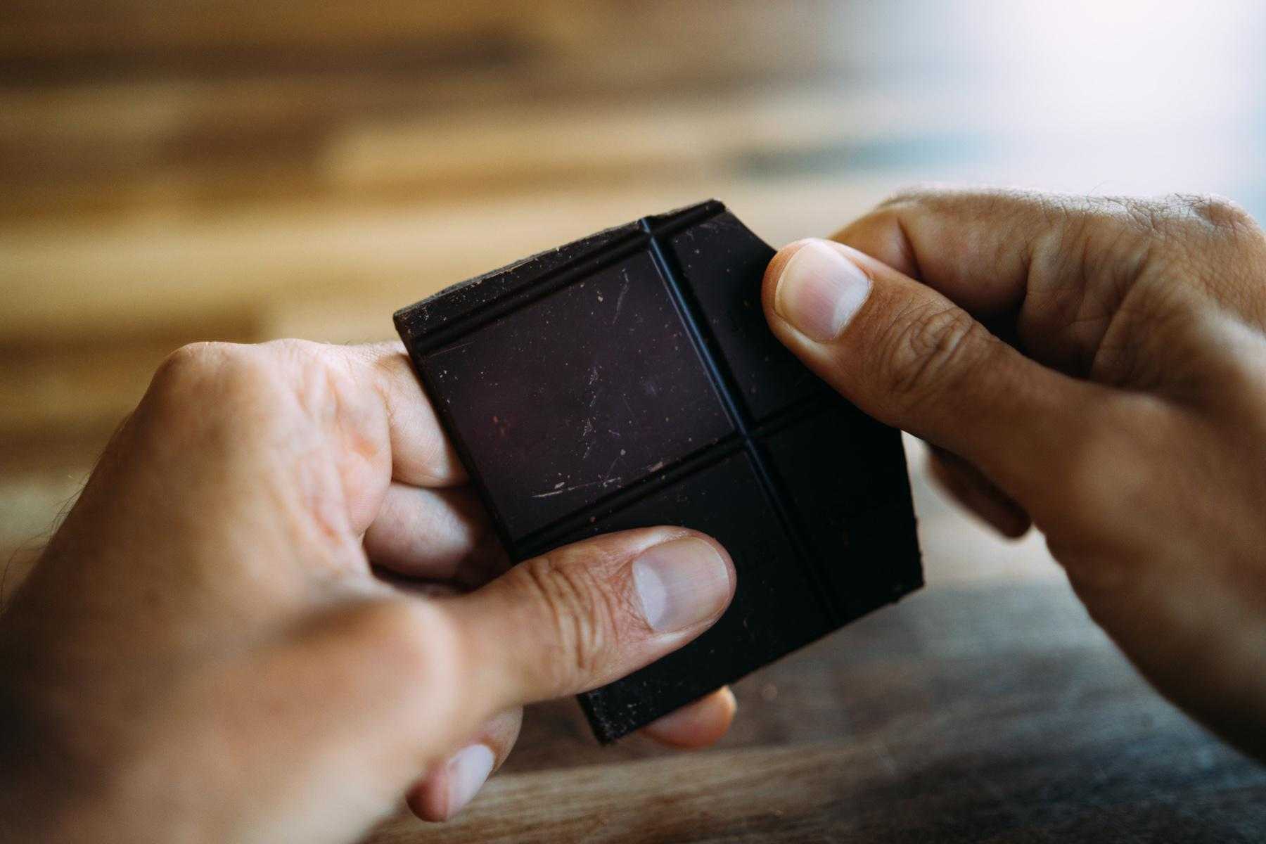 Close-up of man breaking apart bar of dark chocolate.