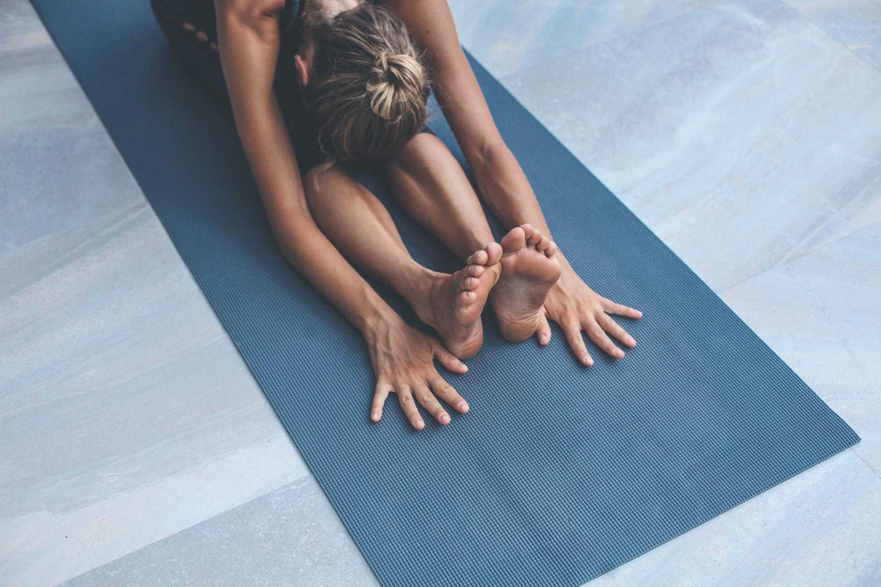 close-up of woman on dark blue yoga mat in a full forward fold