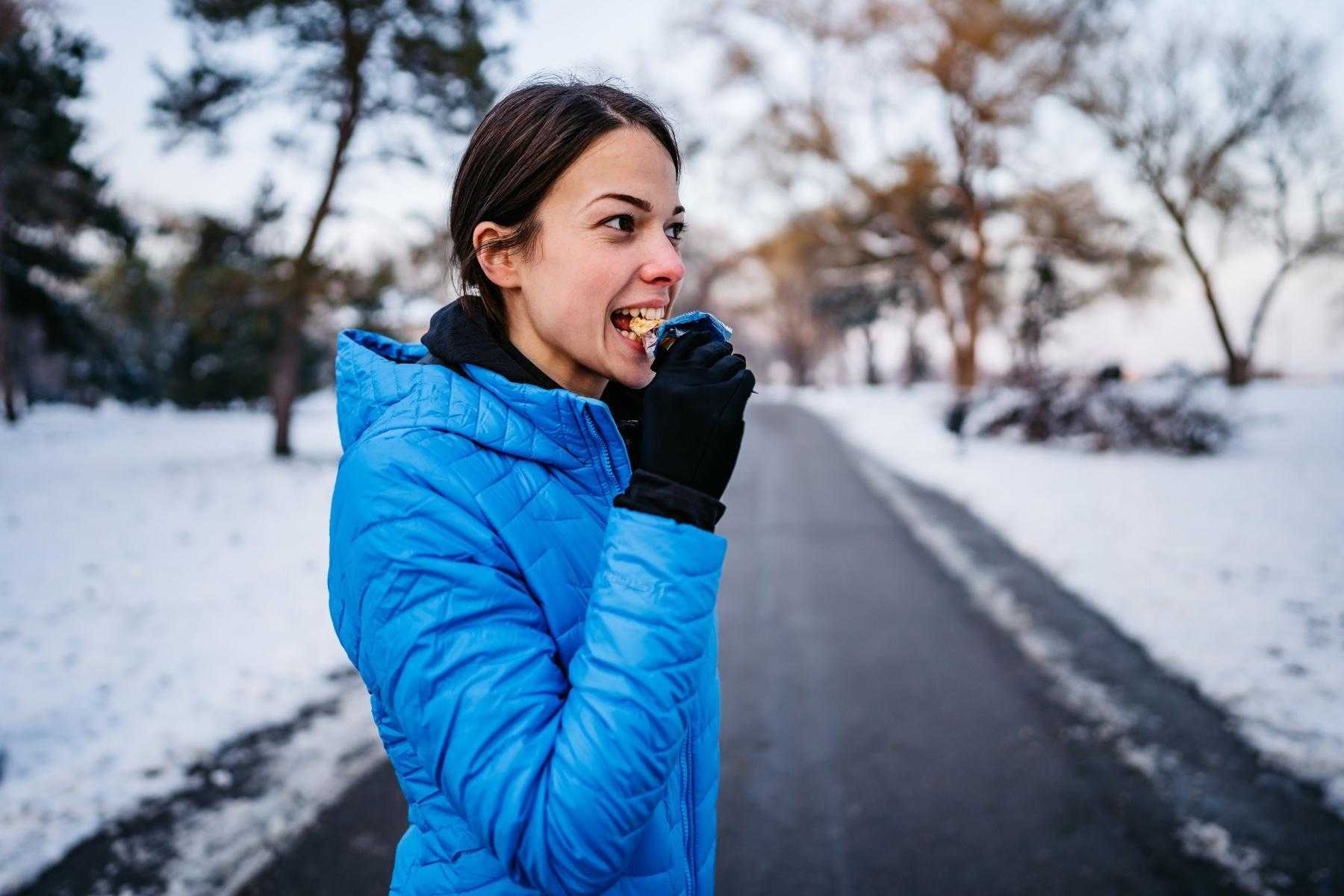 woman eating energy bar on winter trail