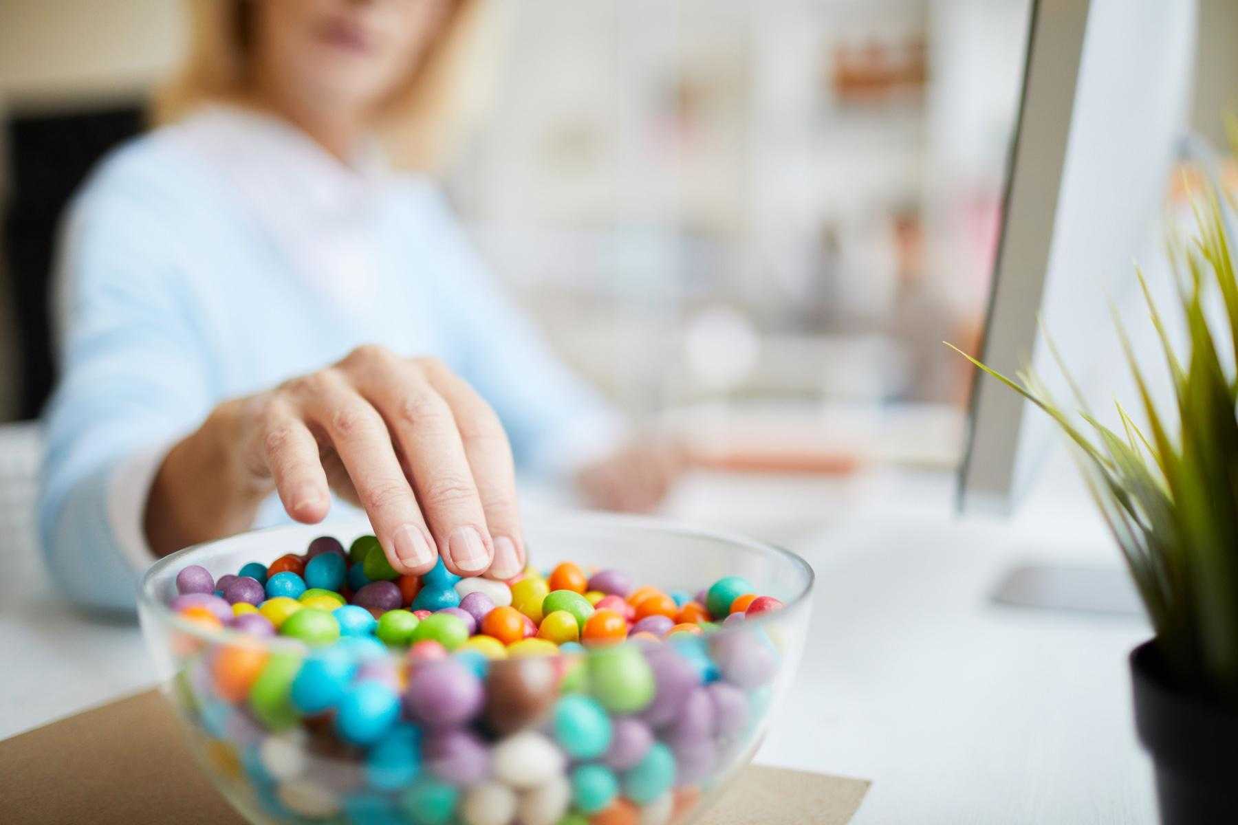 Close-up of woman sticking hand into bowl of candy.