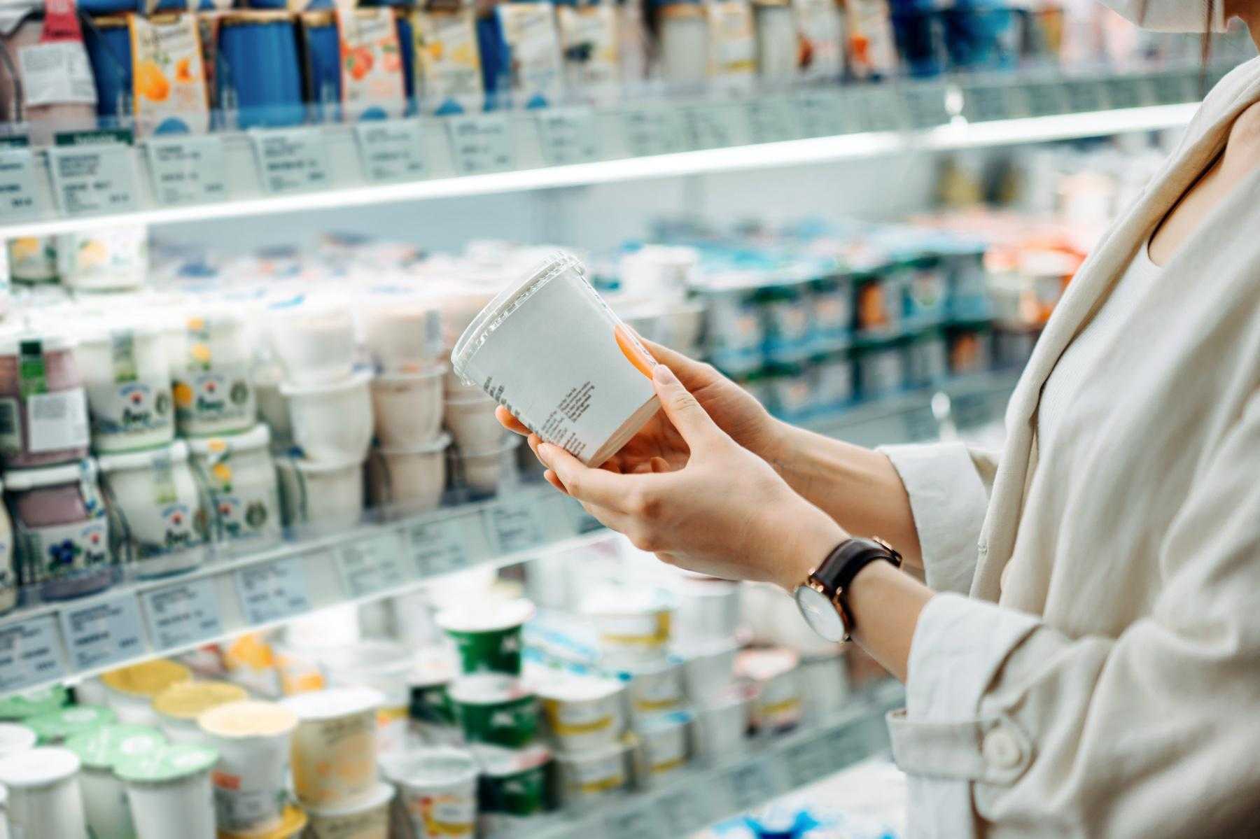 close-up for woman from shoulders down reading nutrition label on yogurt in yogurt section of grocery store