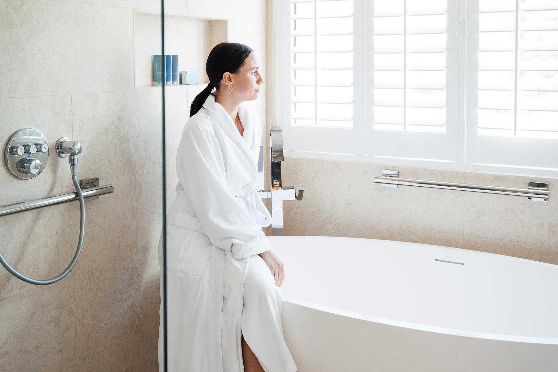 A woman standing in a Canyon Ranch Tucson suite bathroom next to the bathtub.