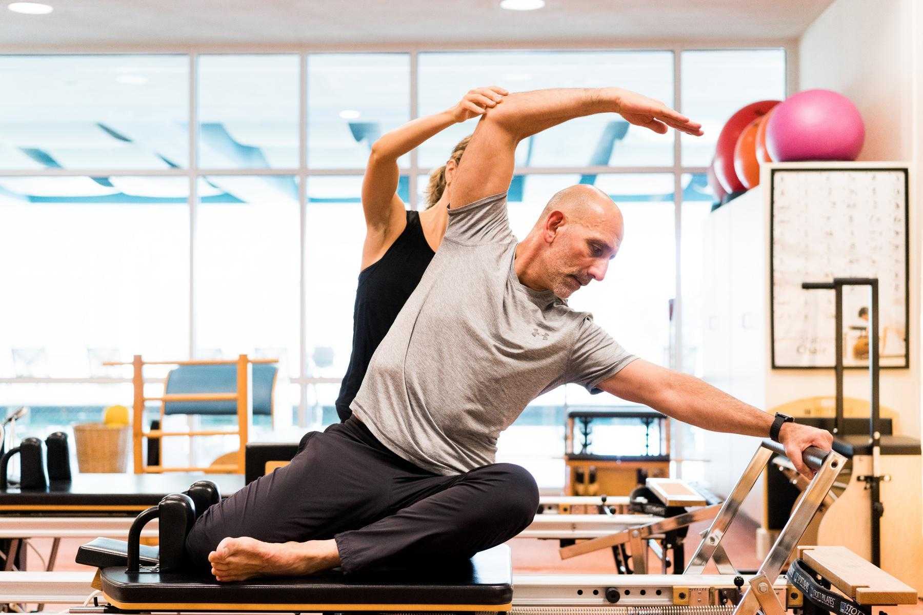 man being guided on pilates reformer machine by woman behind him