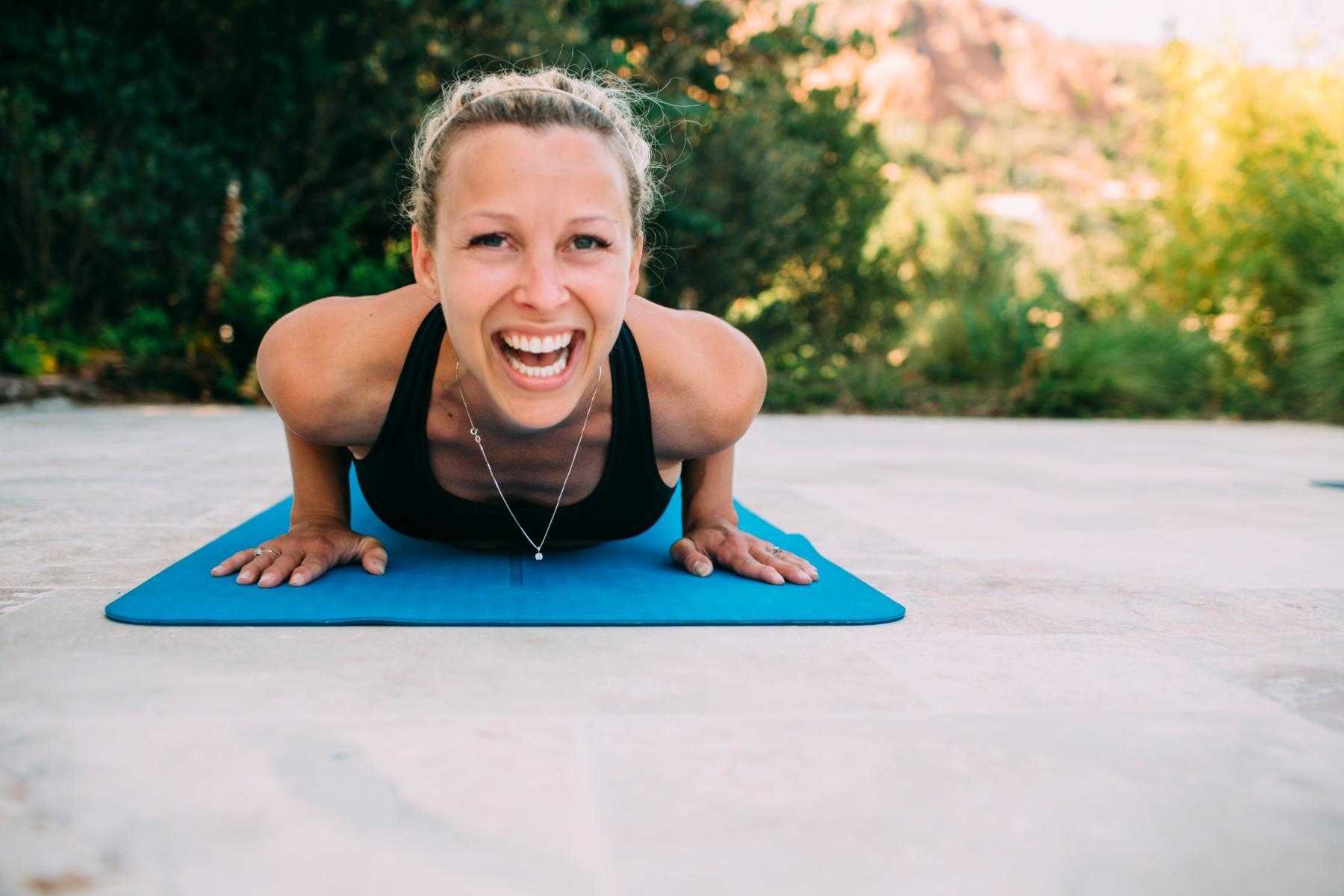 close-up of woman's face as she laughs while laying on yoga mat outside