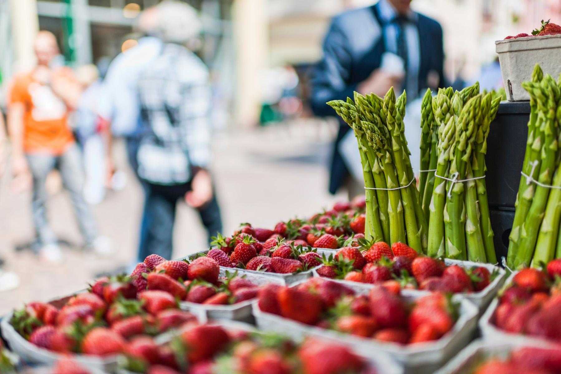 Close-up image of fresh strawberries and asparagus on a table at a farmer's market.