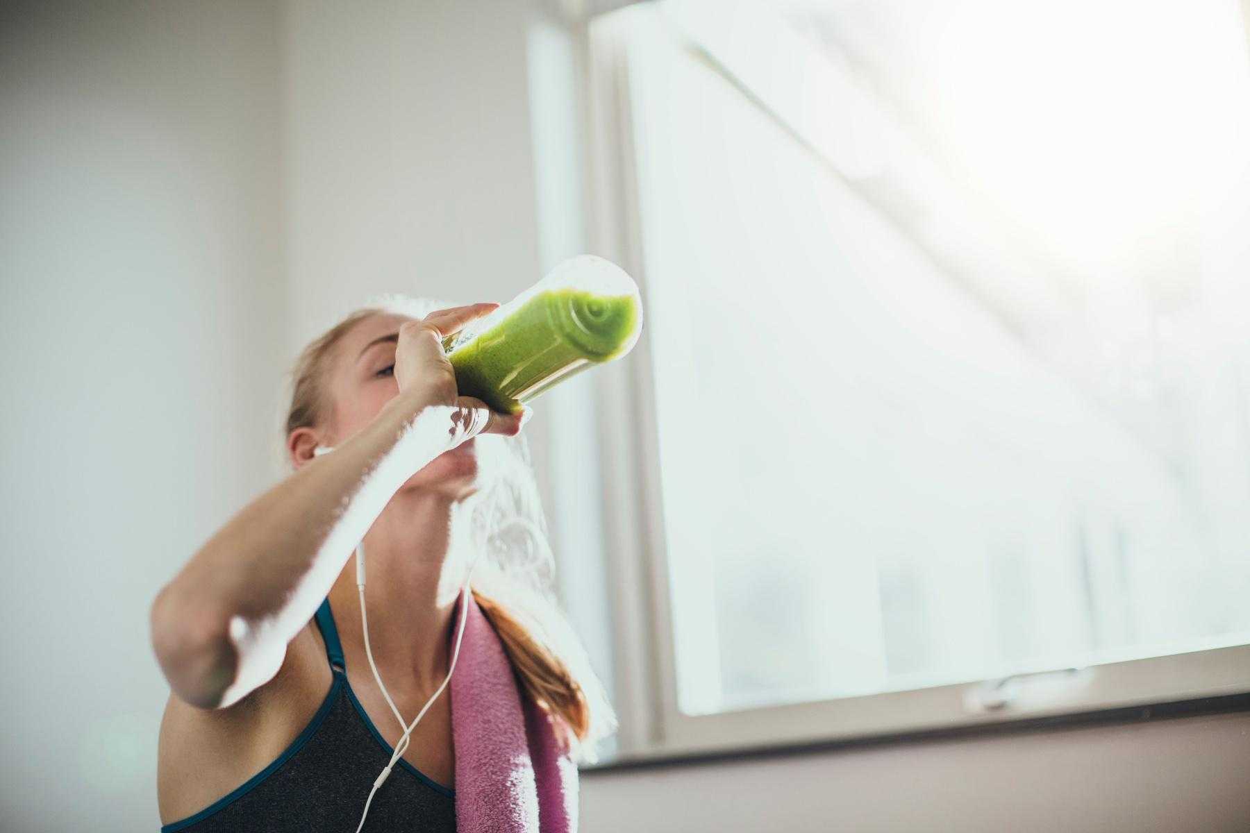 woman drinking green juice after finishing workout