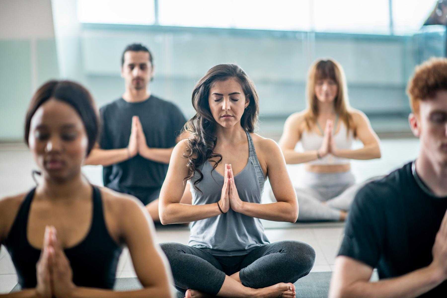 A meditation class with their hands in prayer mudra position.