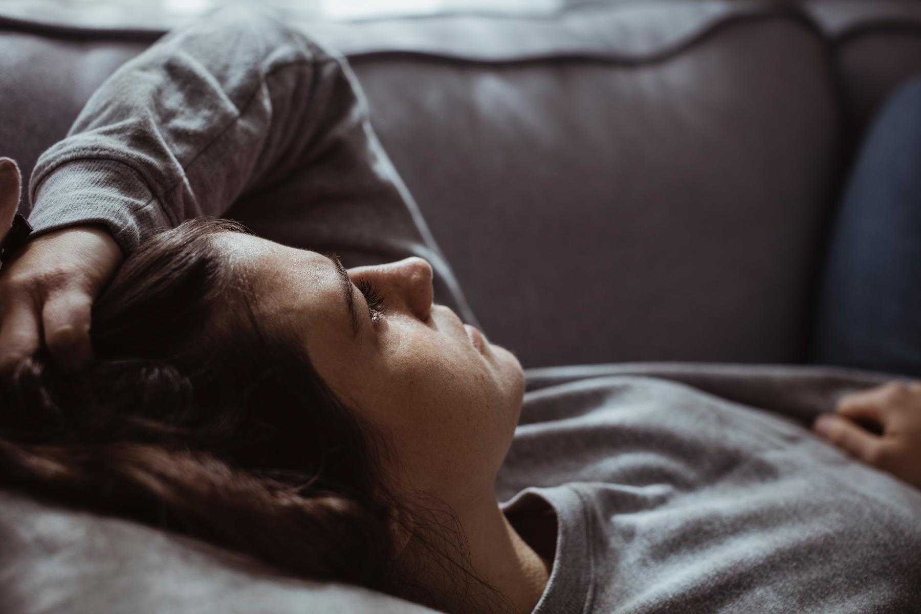 Close-up of stressed out woman laying on couch with her hand in her hair.