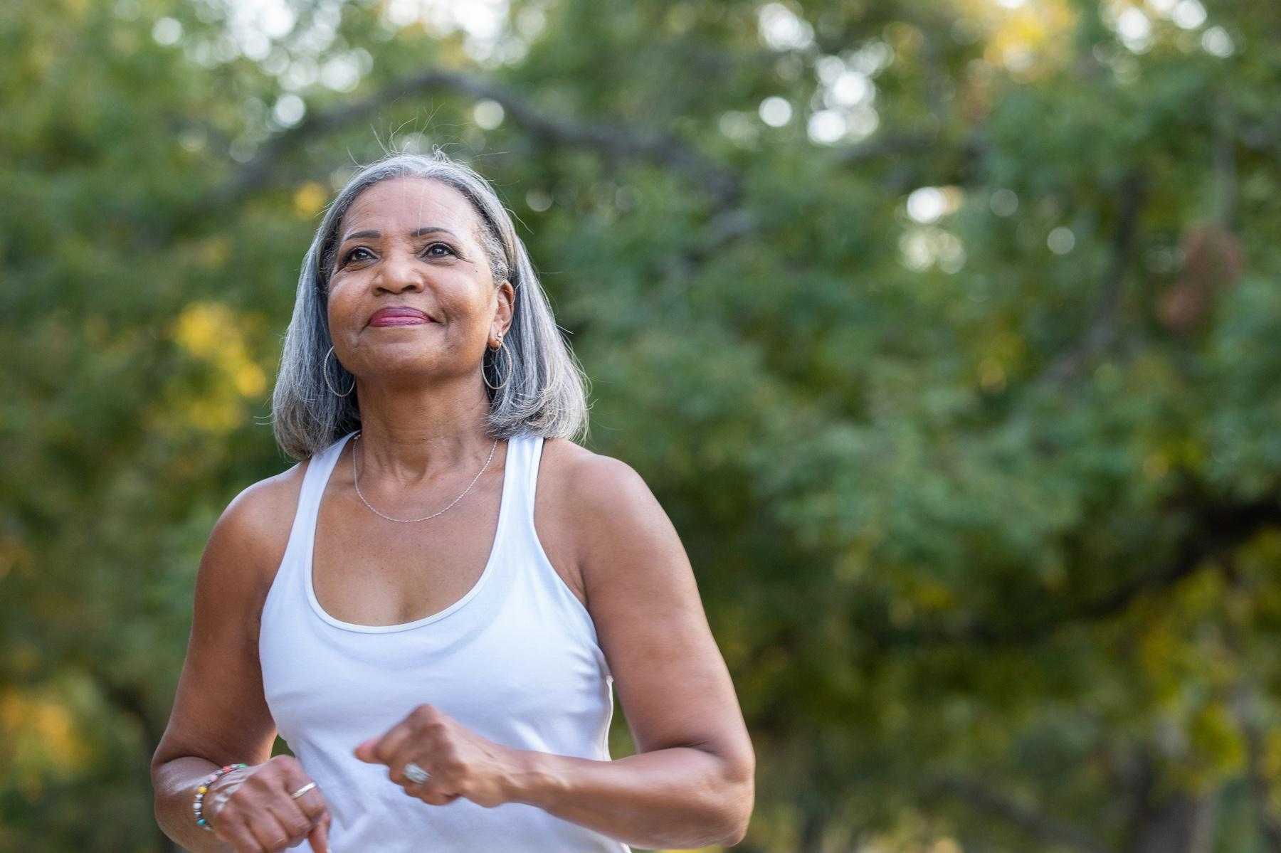 older woman shown from waist up power walking with green tree background
