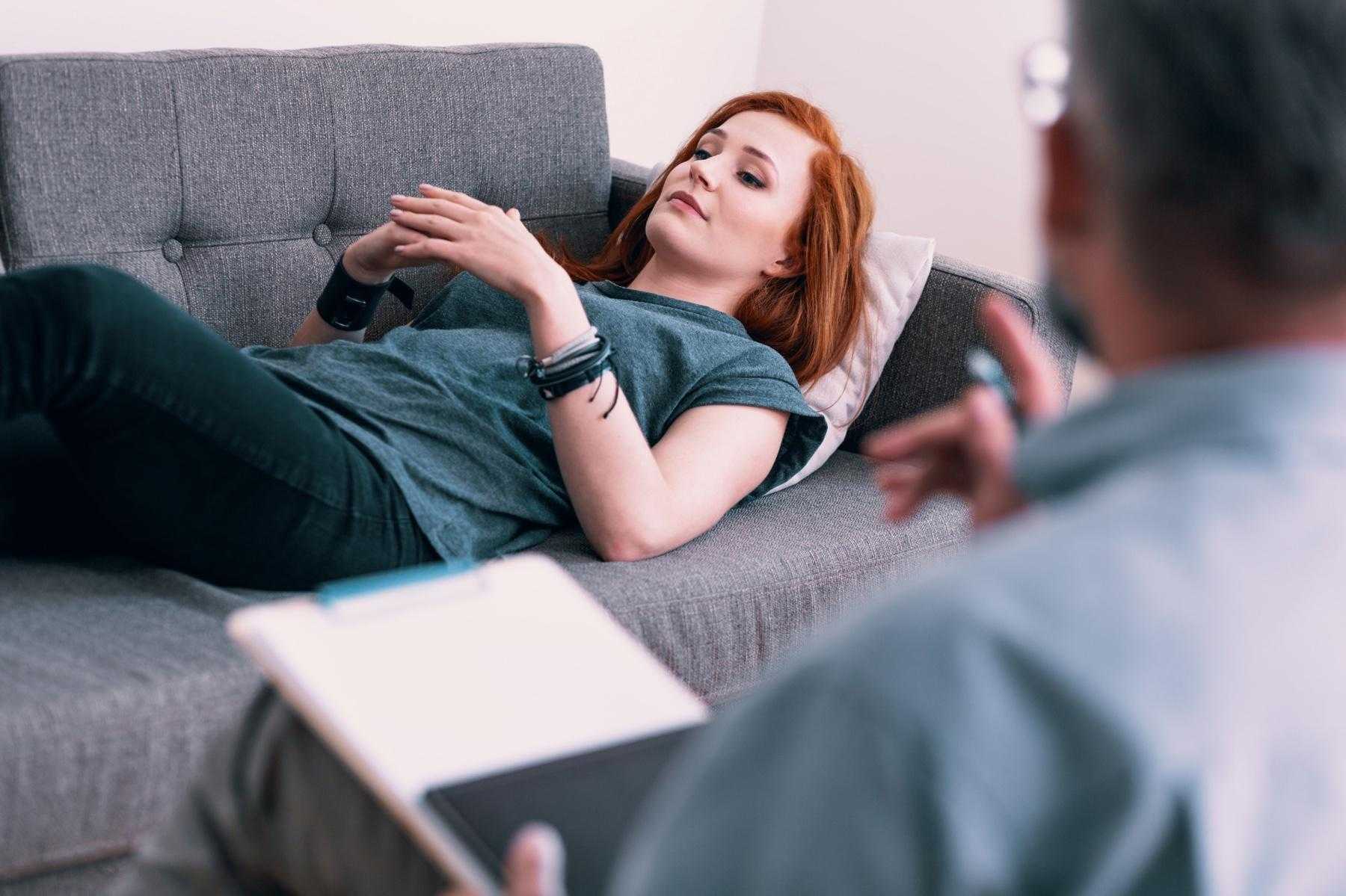 A woman lying on a couch while speaking with her therapist.