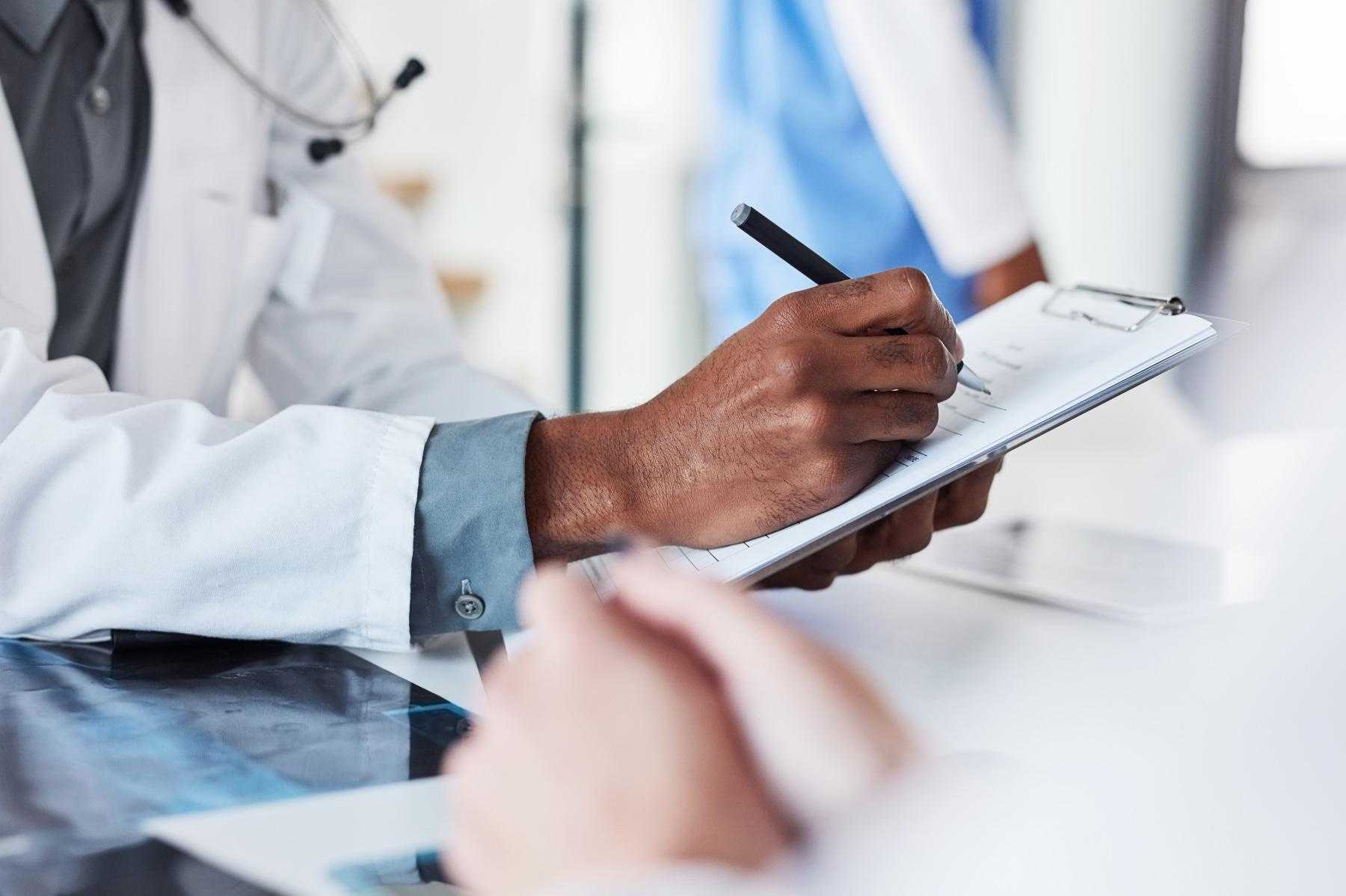 Close-up of doctor's hand writing on clipboard with pen.